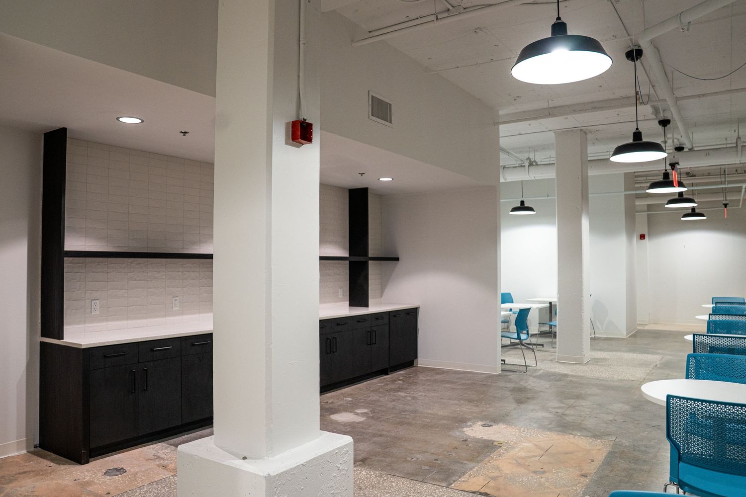 Minimalist office interior with white columns and industrial black pendant lighting fixtures.