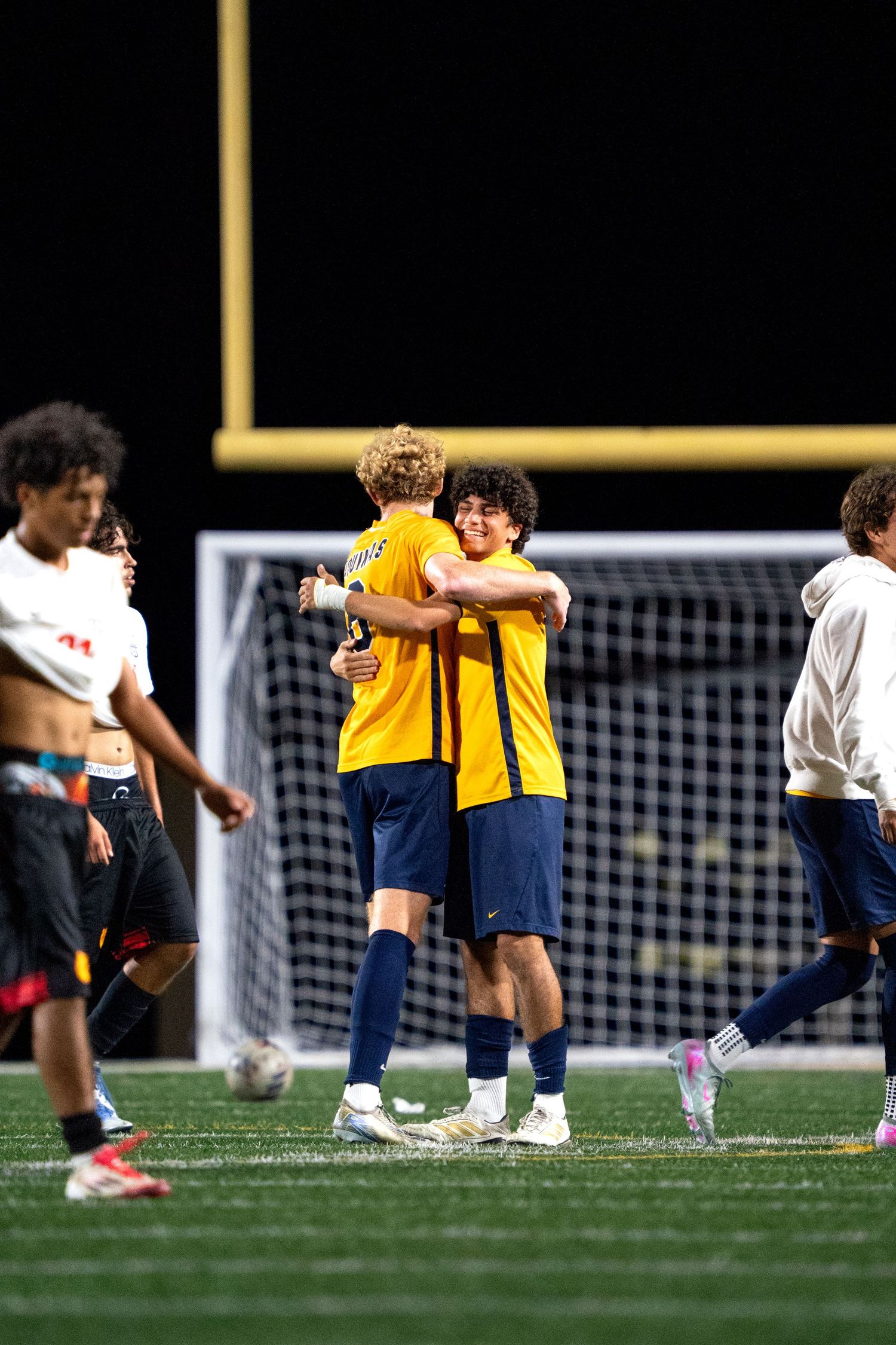 Soccer teammates in yellow jerseys embracing after game on field.