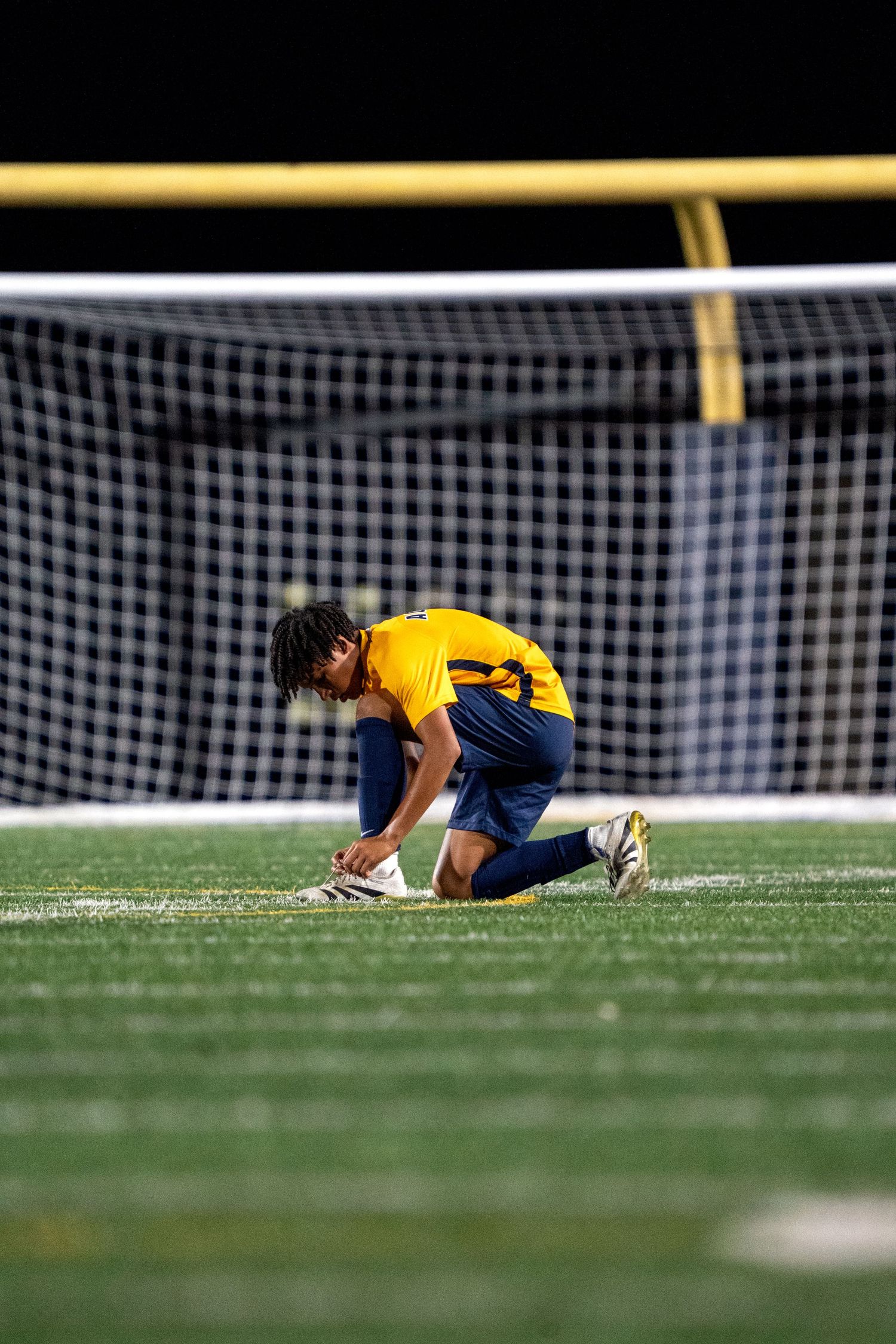 Soccer player in yellow jersey dives near goal post during match.