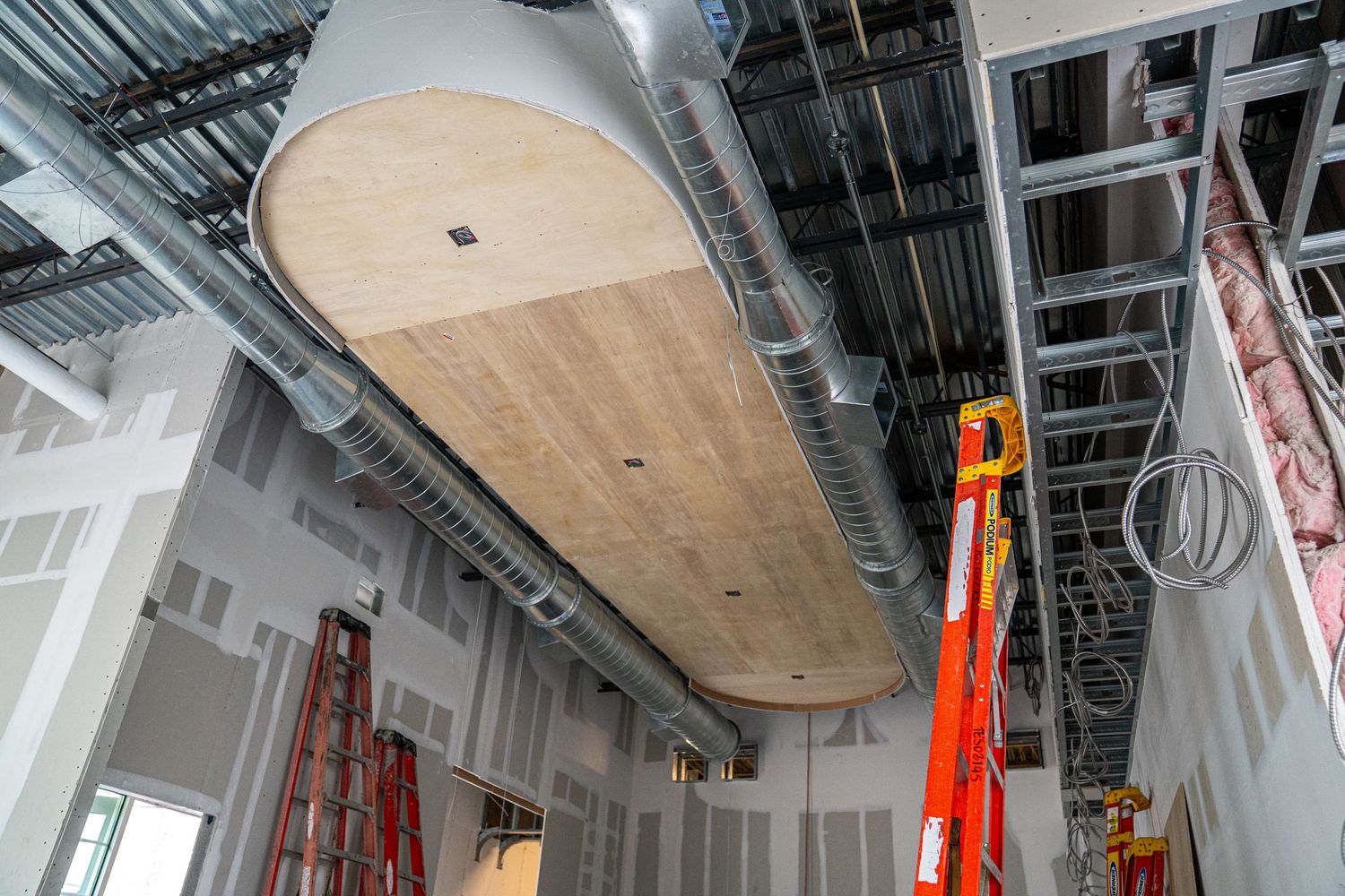 Wooden panel installed on ceiling with exposed mechanical systems and orange lift equipment visible.