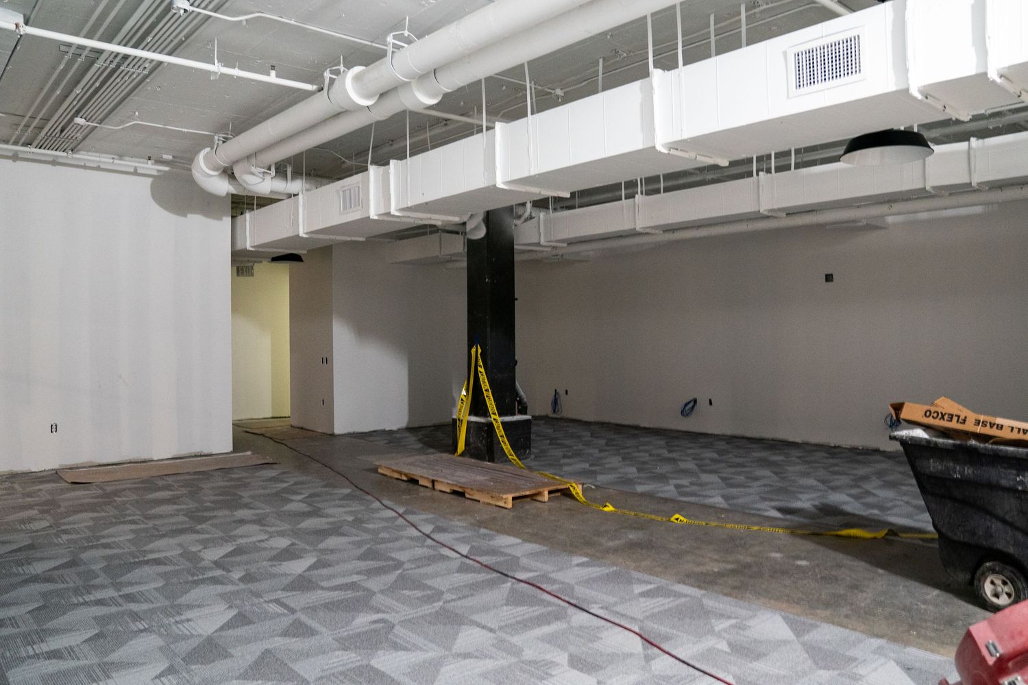 Commercial space renovation showing new flooring installation and exposed ceiling ductwork.