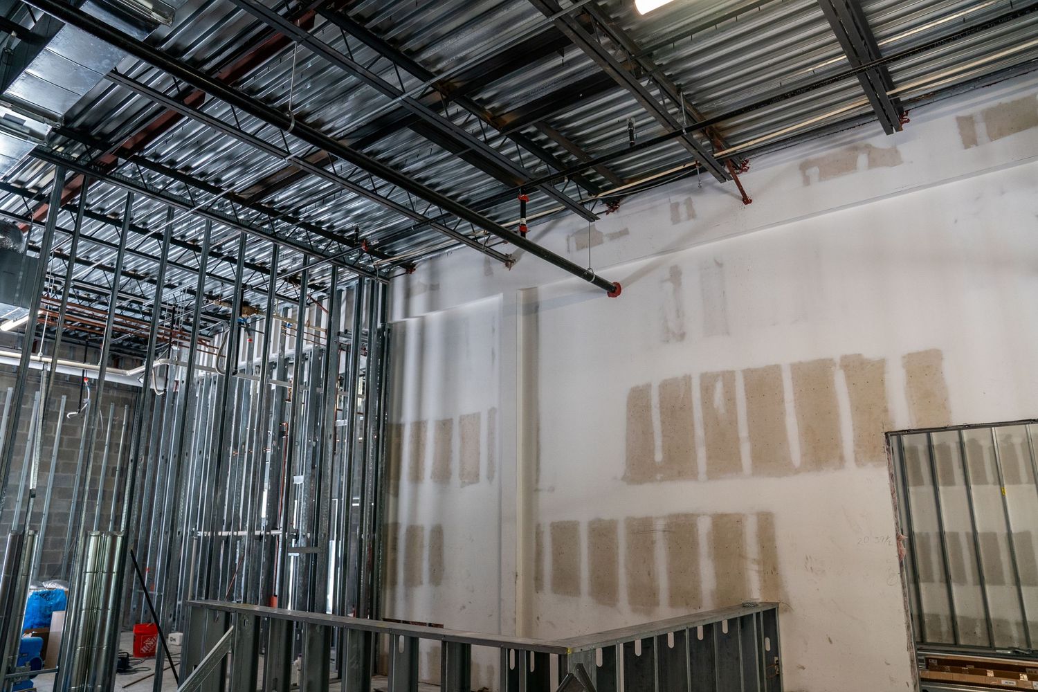 Partially completed drywall installation showing metal framing and exposed ceiling infrastructure.