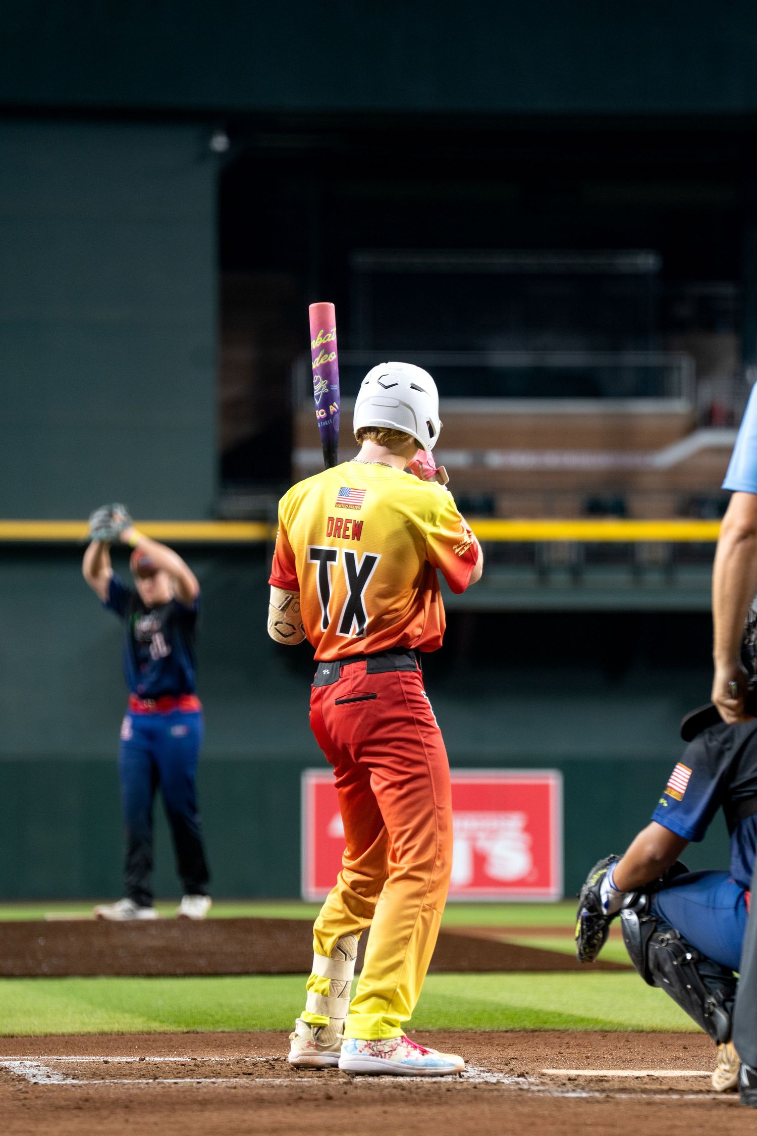 Baseball player in orange uniform swings bat during game while catcher crouches behind home plate.