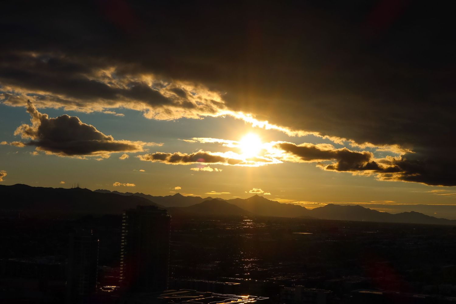 Dramatic sunset over city skyline with dark clouds and golden sunlight breaking through.