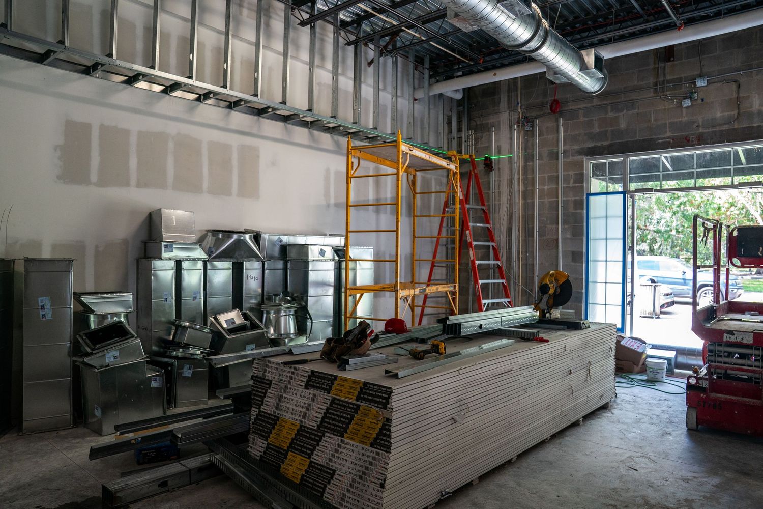 Construction site interior with ladders, tools, and ongoing drywall installation work.