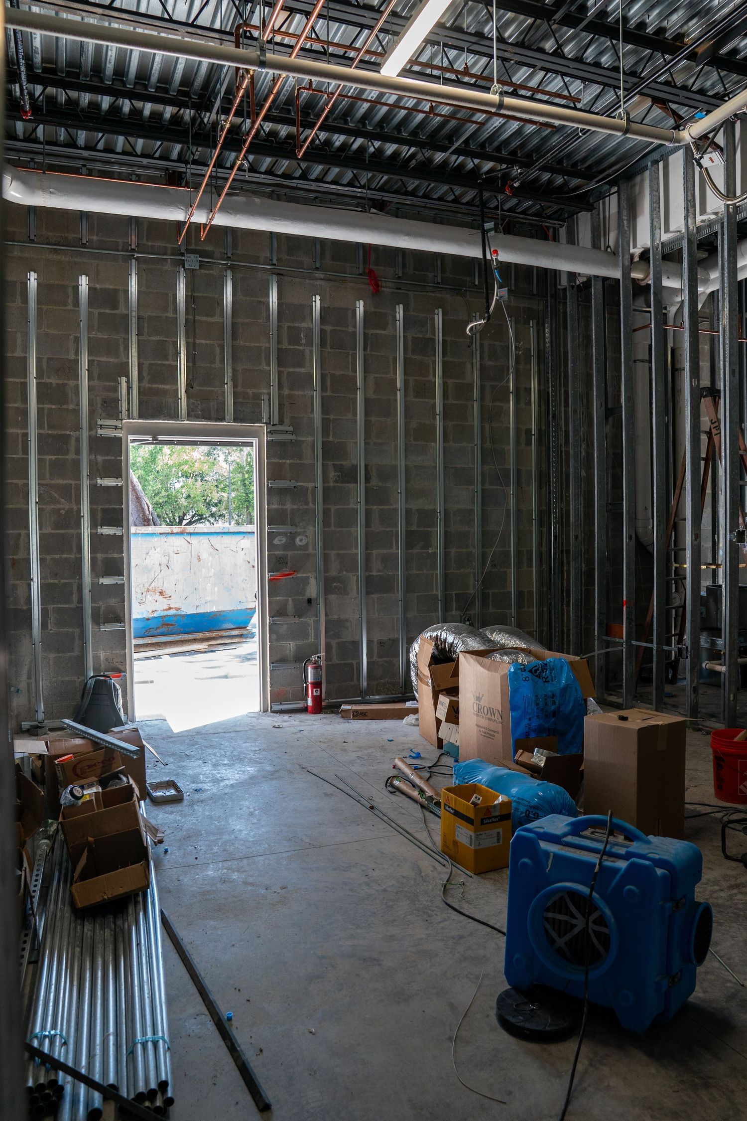 Unfinished commercial space with exposed metal studs and construction equipment on concrete floor.