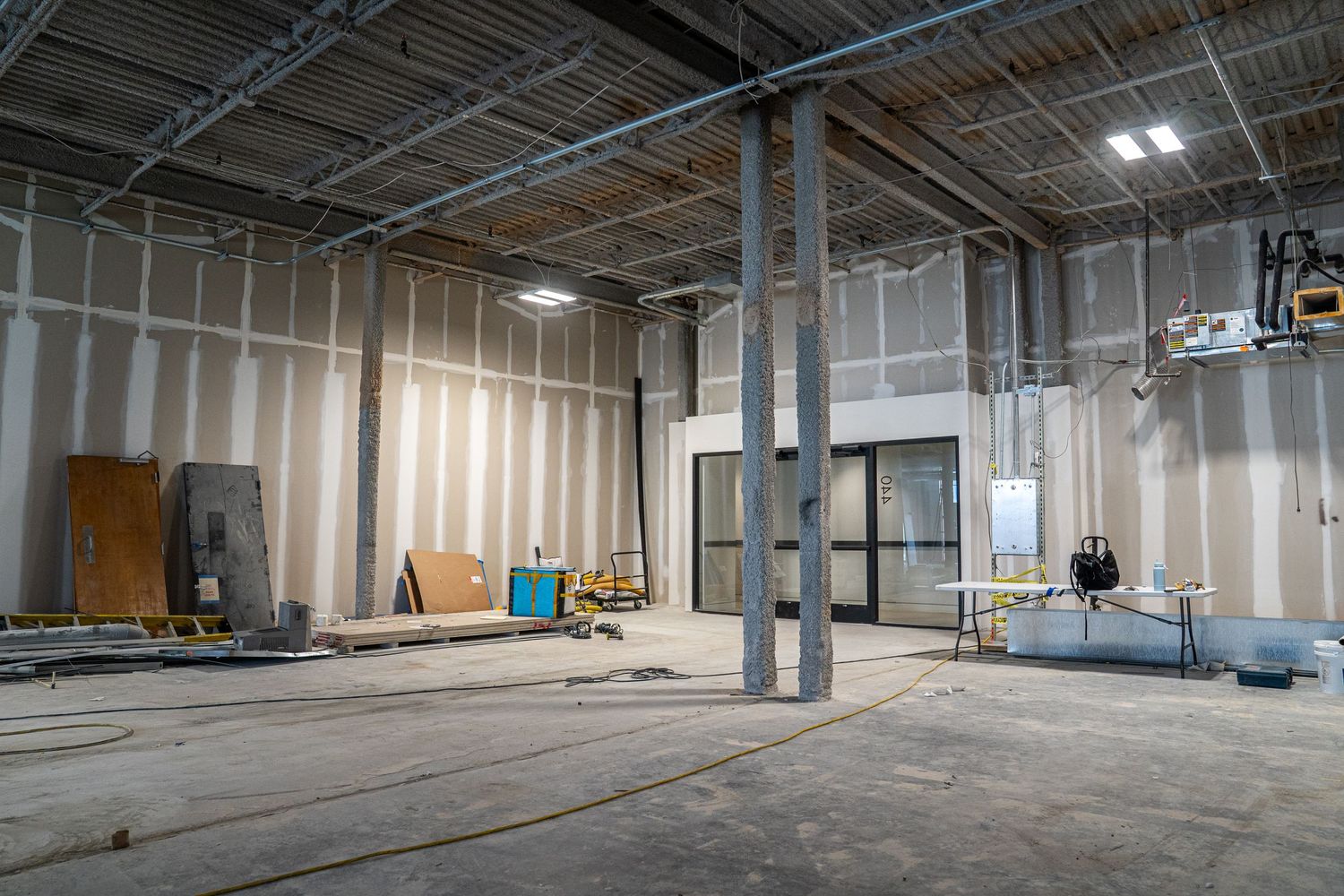 Unfinished commercial interior with metal support beams and white drywall installation in progress.