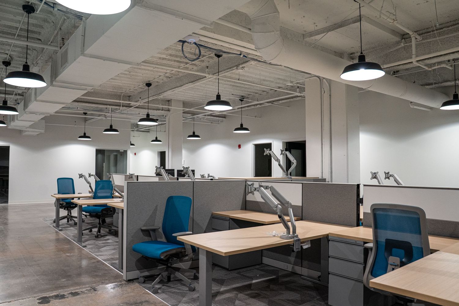 Empty office space with white walls, exposed ductwork, and pendant lights showing a clean industrial design.