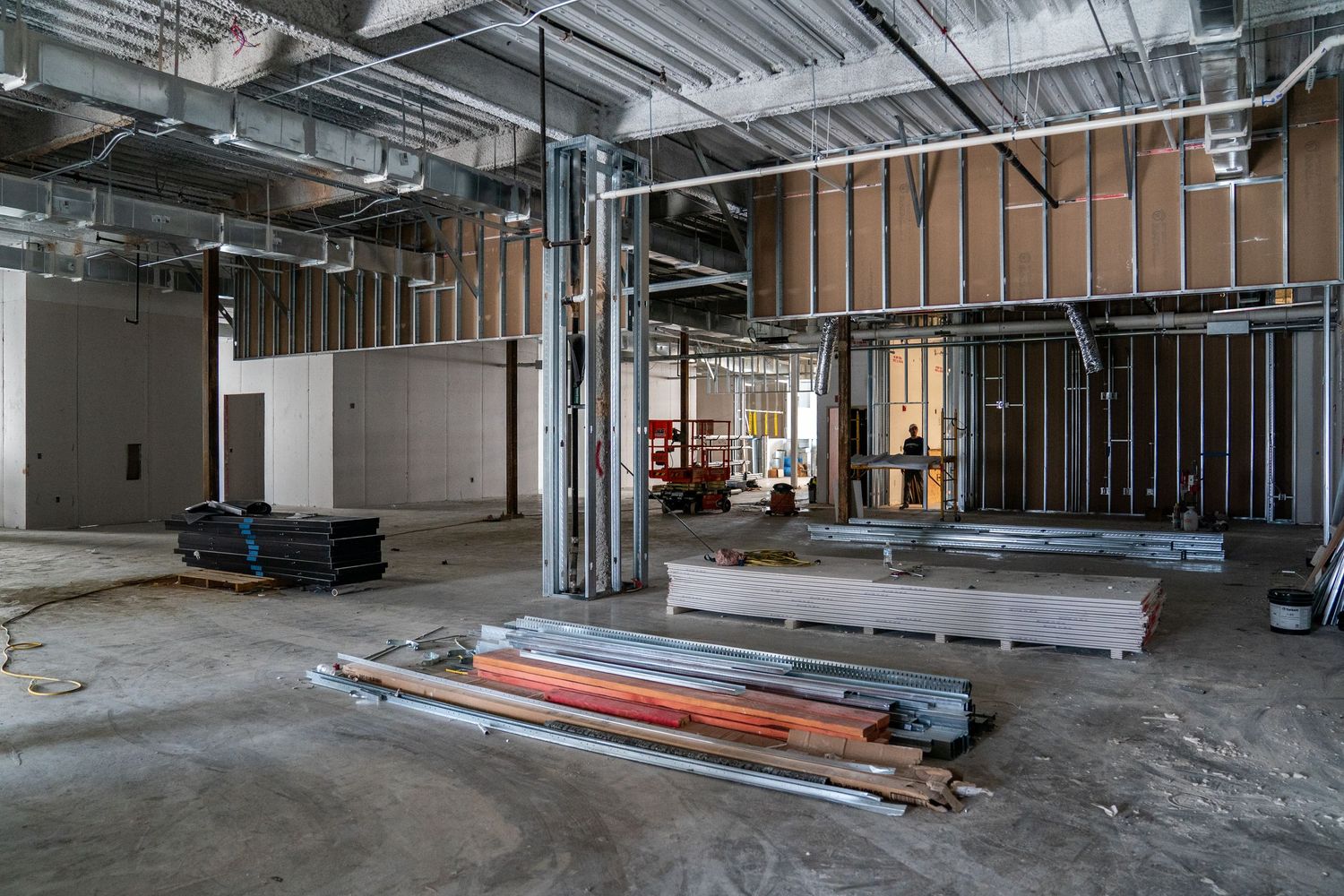 Unfinished commercial interior with metal studs, drywall, and construction supplies spread across concrete floor.
