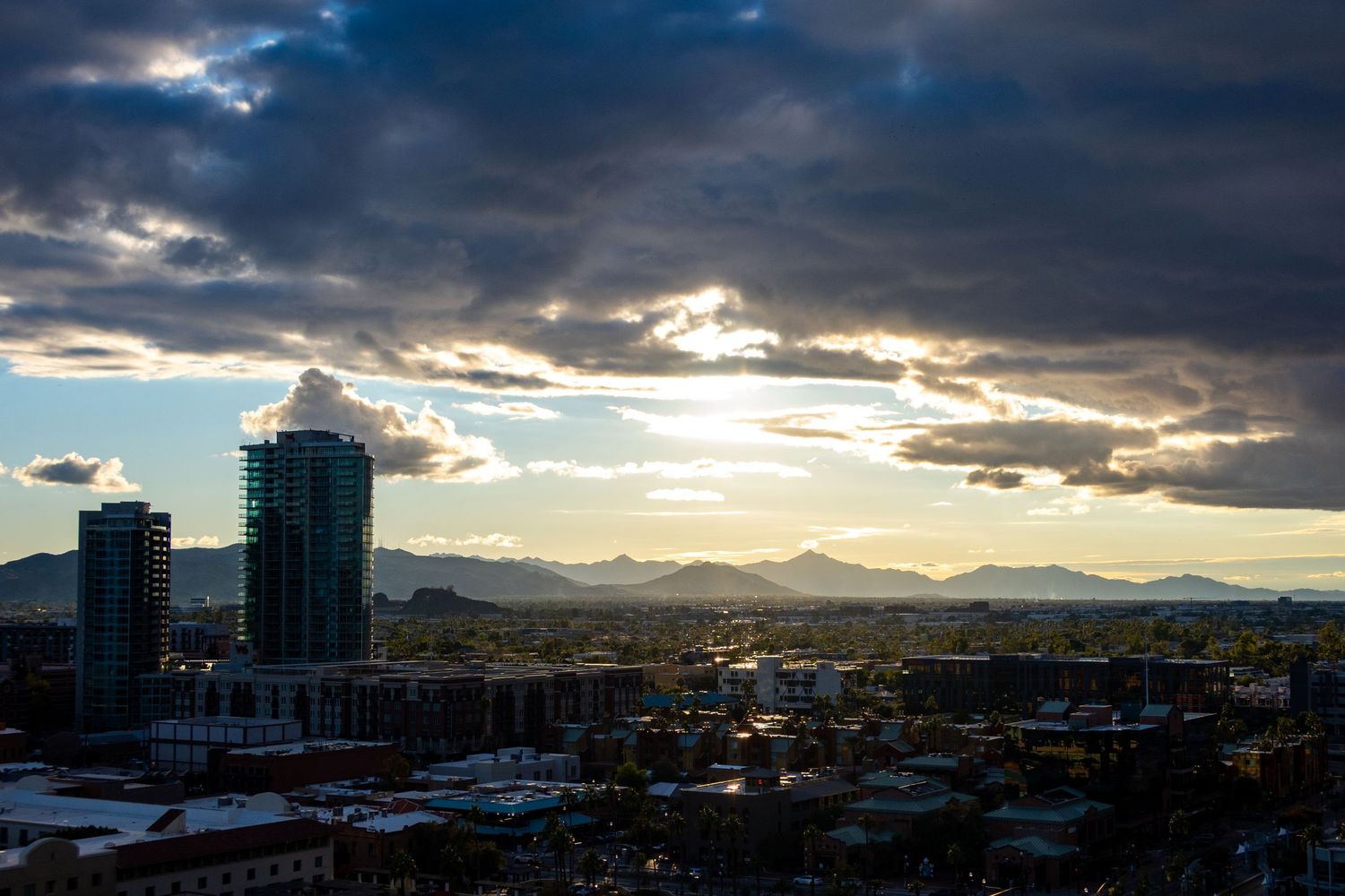 Panoramic view of a city with mountains in background under stormy evening sky.