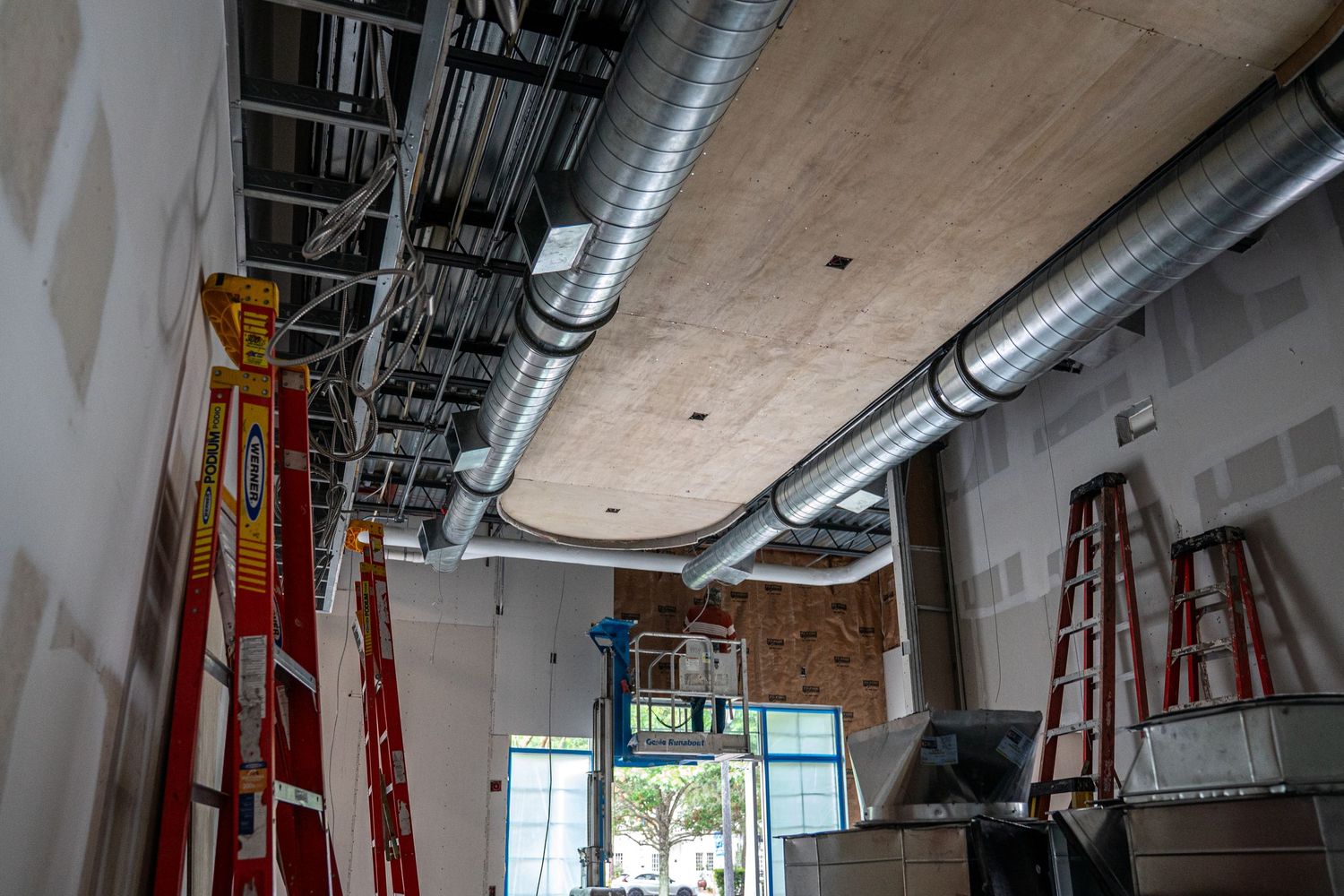 Industrial space renovation showing exposed ceiling infrastructure and construction equipment.
