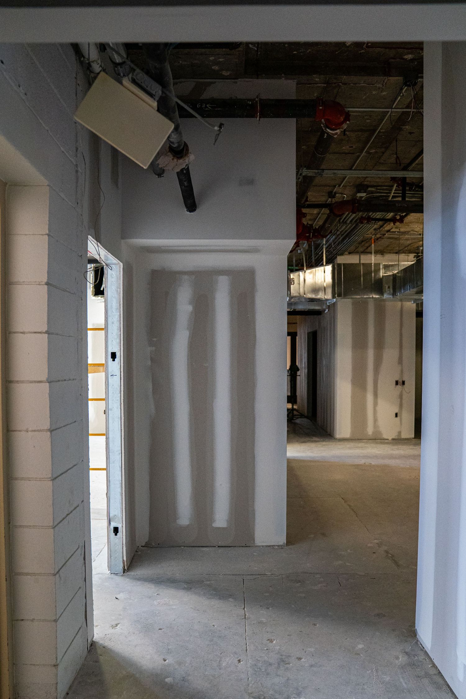 Unfinished commercial interior with white walls and exposed ceiling infrastructure.