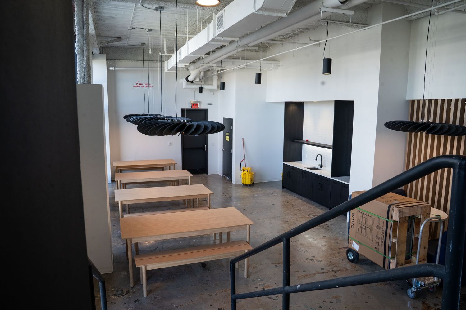 Modern office interior with wooden benches and black railings along a white corridor with industrial ceiling design.