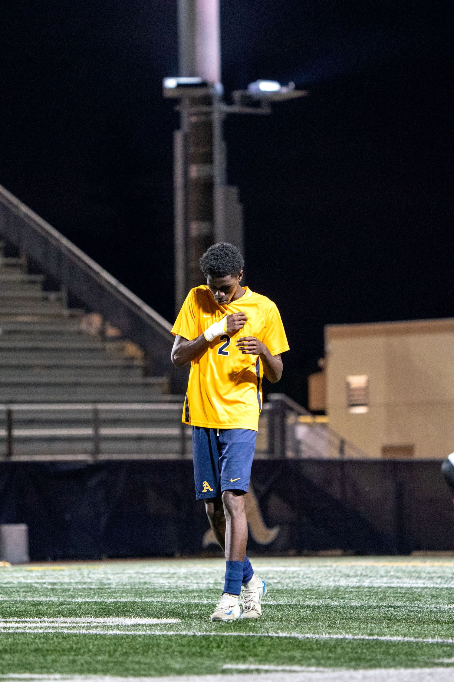 Soccer player in yellow jersey showing emotion on field at night.