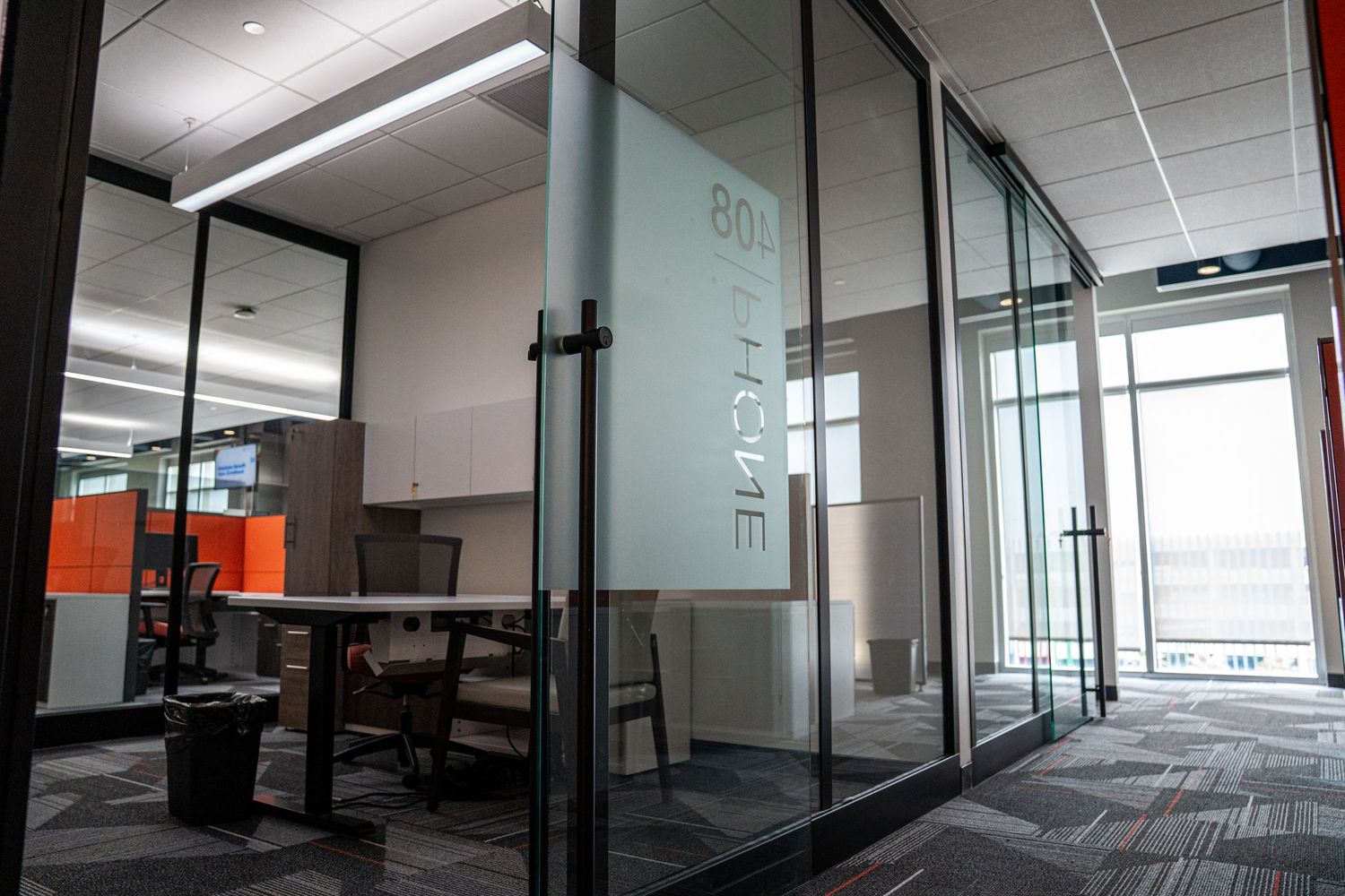 Corporate office space with glass walls, modern workstations, and natural lighting from large windows.