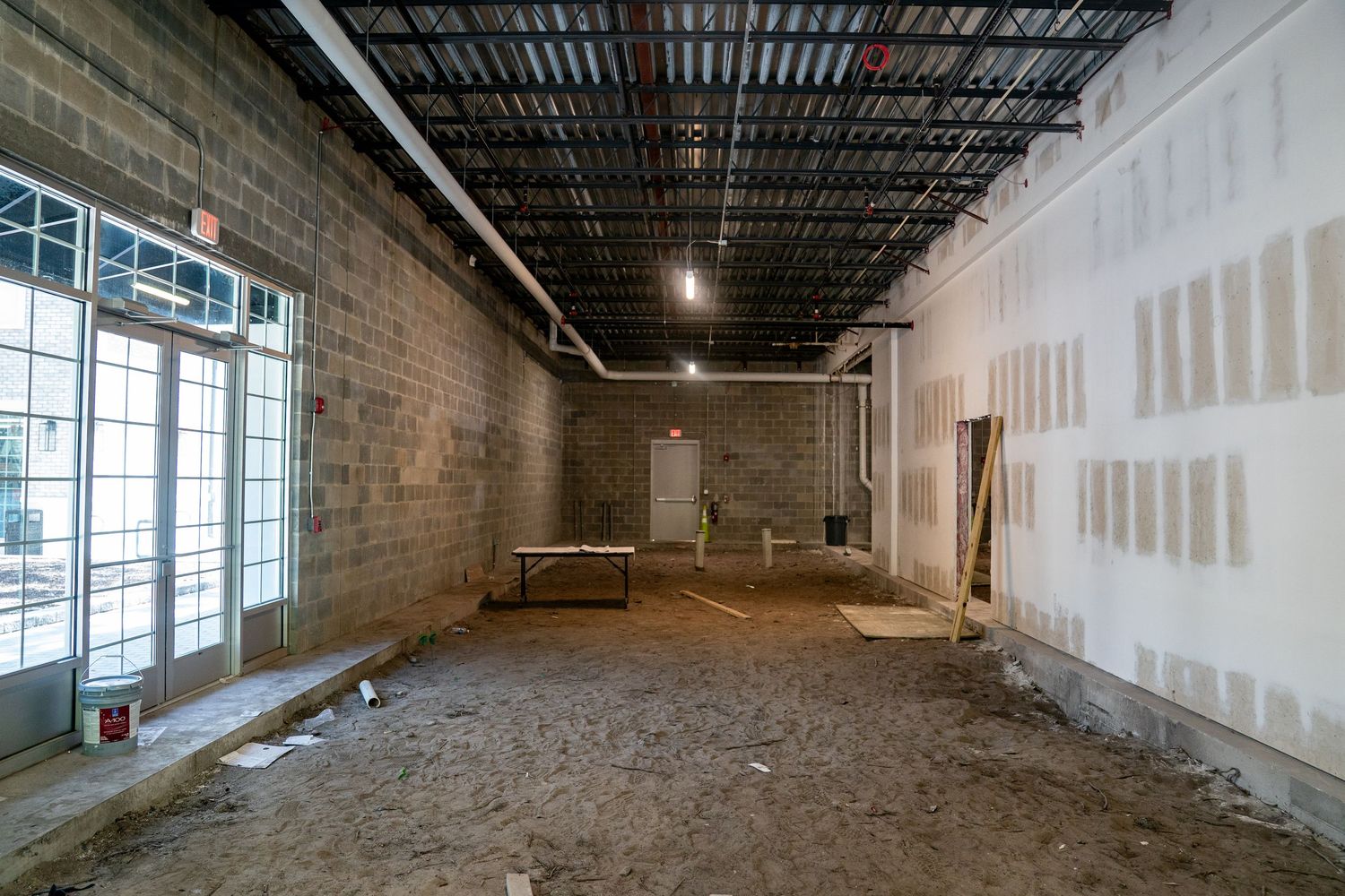 Wide panoramic view of an empty commercial space with exposed ductwork and natural lighting.