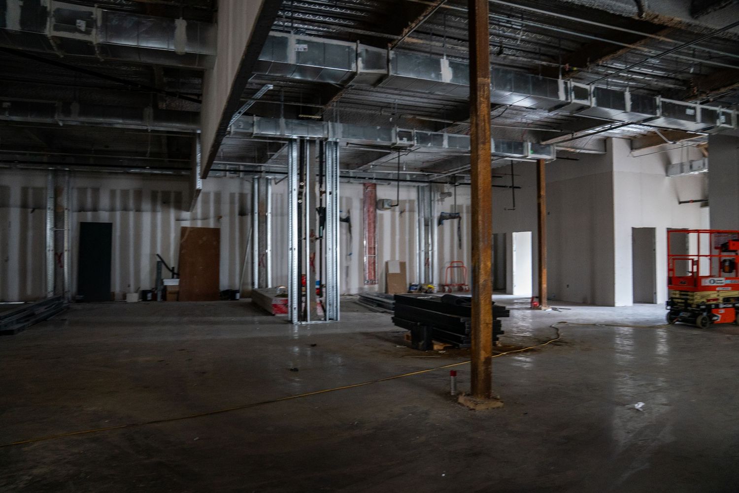 Industrial space under renovation showing exposed ceiling, support columns, and concrete floor.