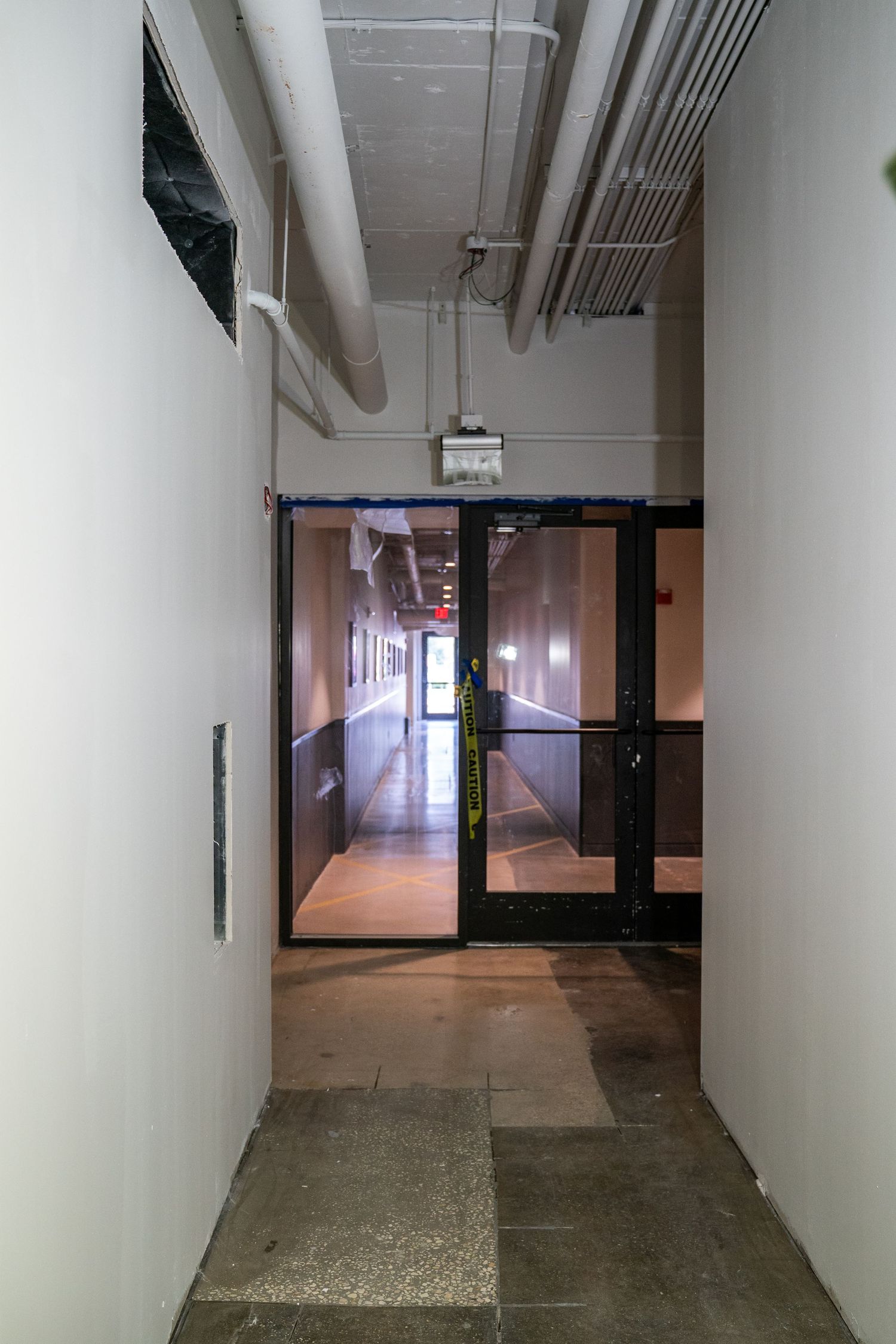 Long industrial hallway with white walls and exposed ceiling utilities shows construction in progress.