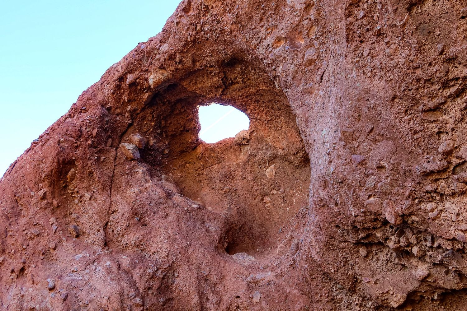 Natural hole formation in red sandstone rock against bright blue sky.