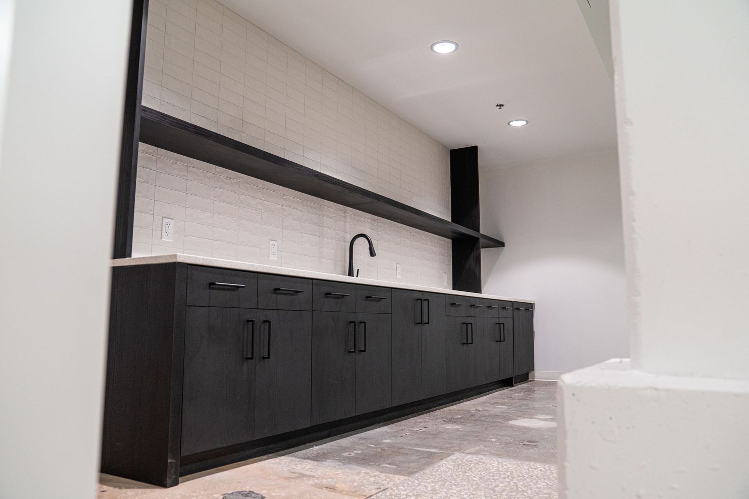 Modern black kitchen cabinets with sink installed against white tile wall.