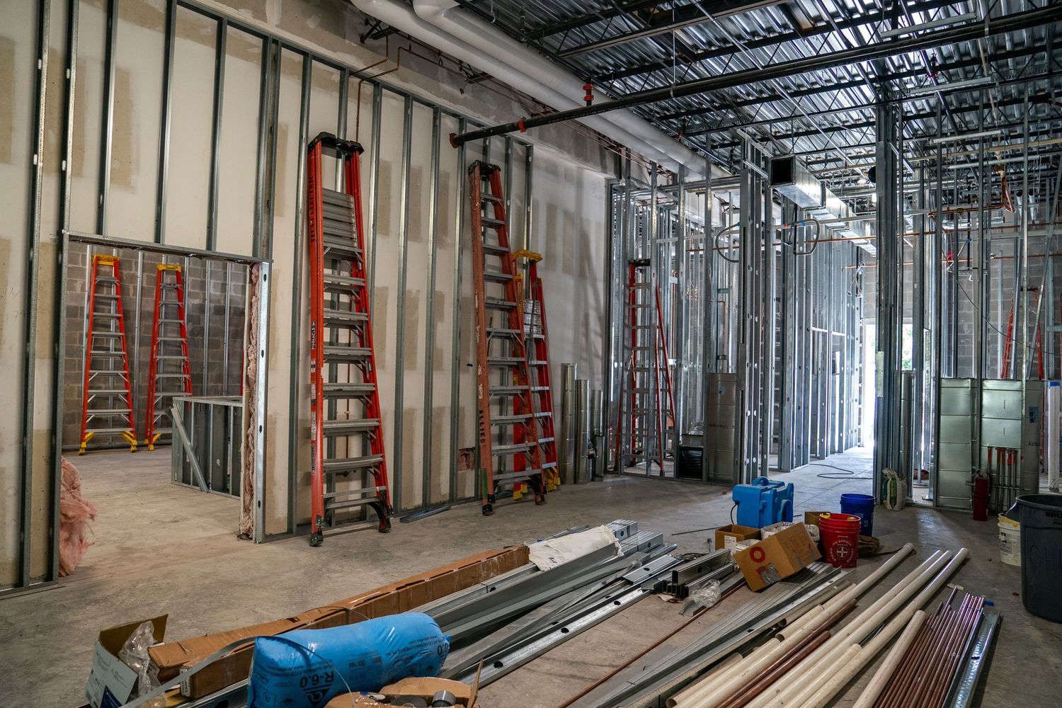 Long view of commercial construction site with metal framing and red ladders along concrete floor.