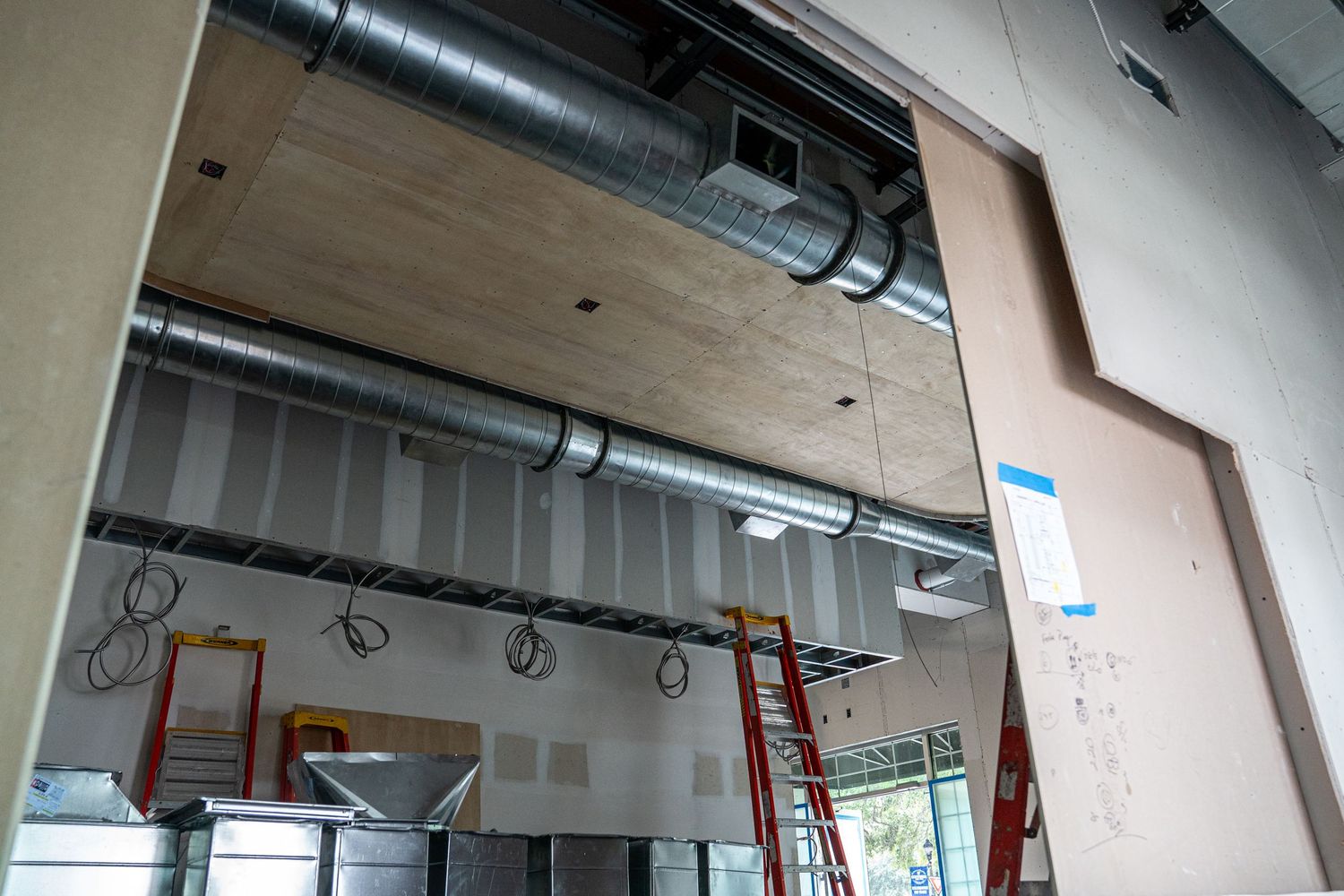 Commercial space under construction showing exposed ceiling ductwork and drywall installation in progress.