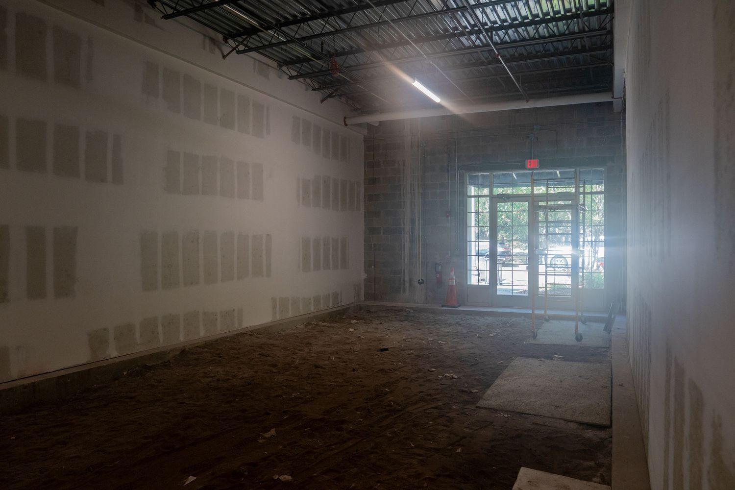 Empty retail space under construction with drywall walls and large windows letting in natural light.