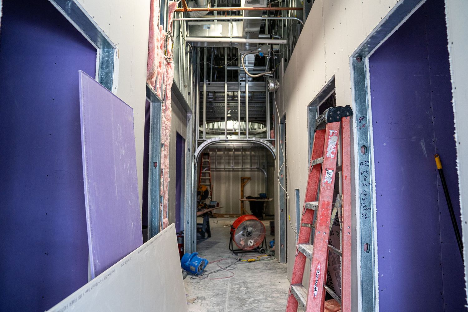 Purple-painted corridor under construction with exposed framing and utility work.