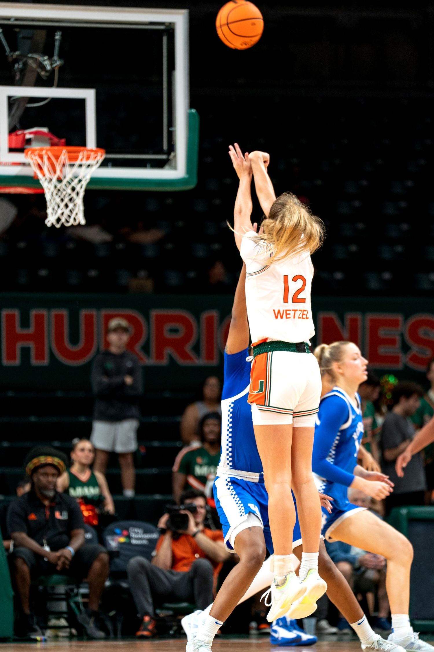 Basketball action shot showing players from both teams jumping for the ball near the hoop.