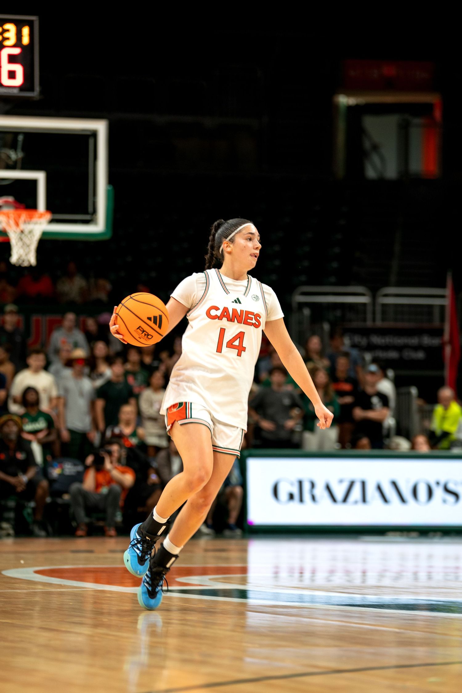 Player in white Canes jersey makes athletic move while dribbling basketball.