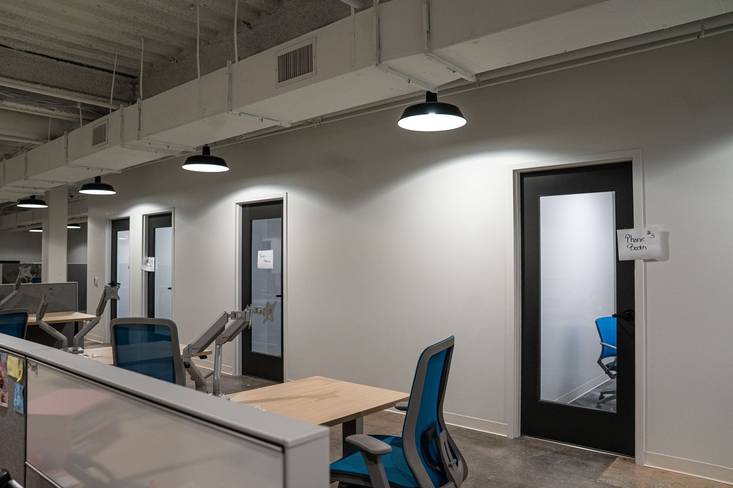 Contemporary office space featuring black doors, blue task chairs, and minimalist workstations.