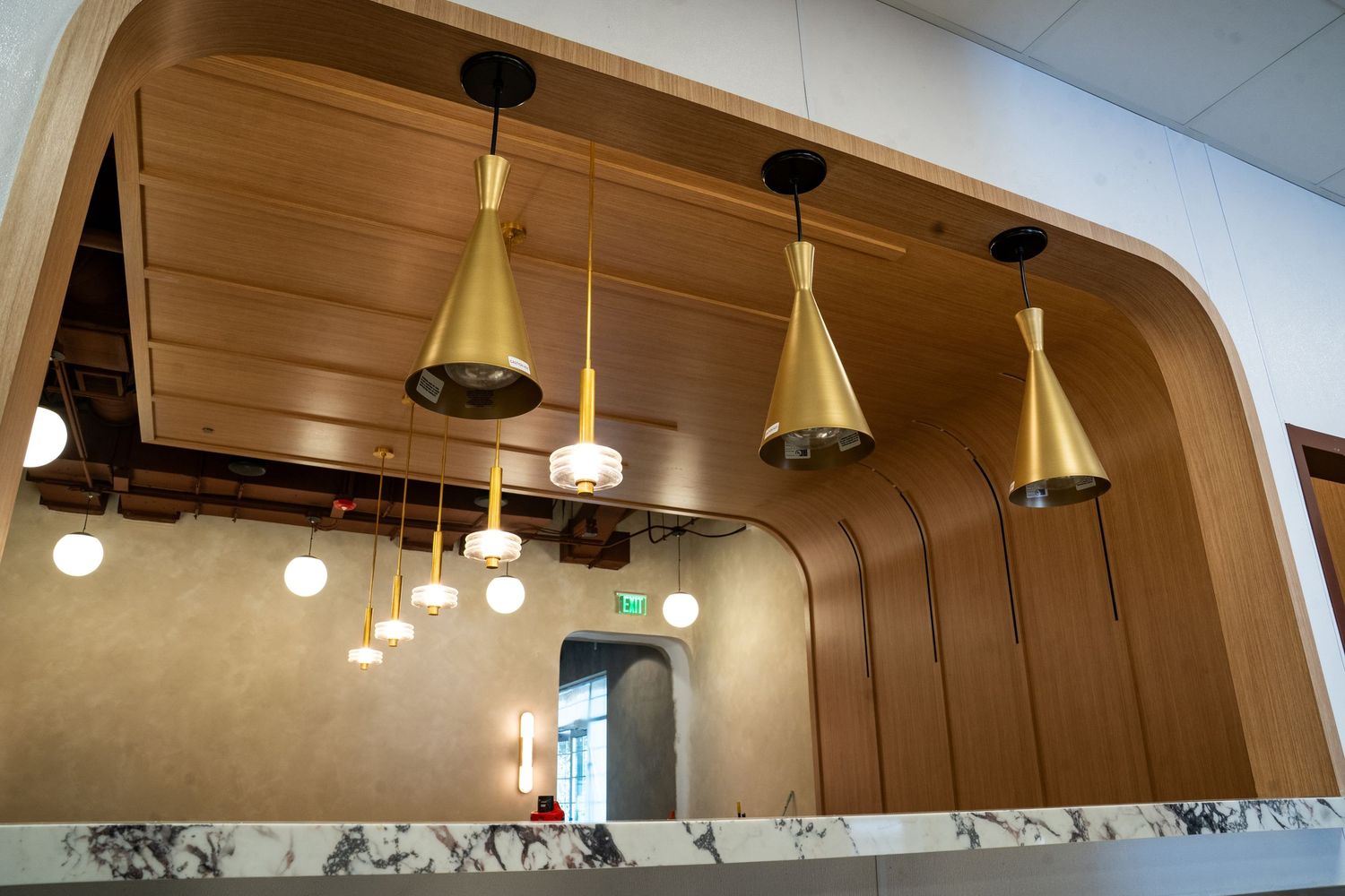 Modern restaurant interior with hanging brass pendant lights and track lighting illuminating a curved ceiling design.