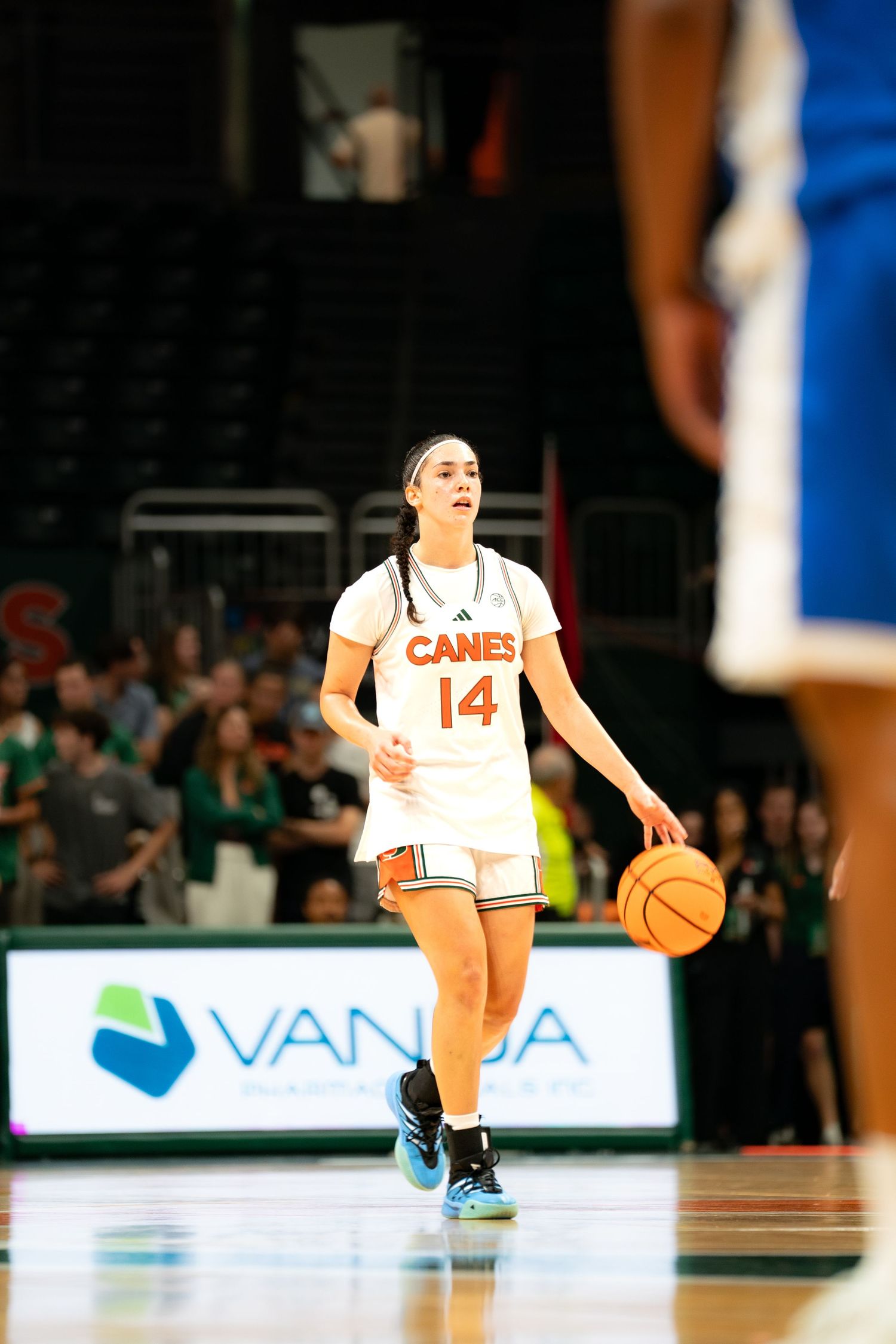 Basketball players in white uniforms with orange 'Canes' text dribble on court.