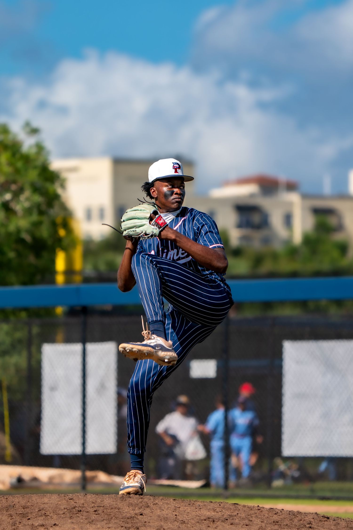 Baseball pitcher in pinstripe uniform winds up for a pitch during a game on a sunny day.