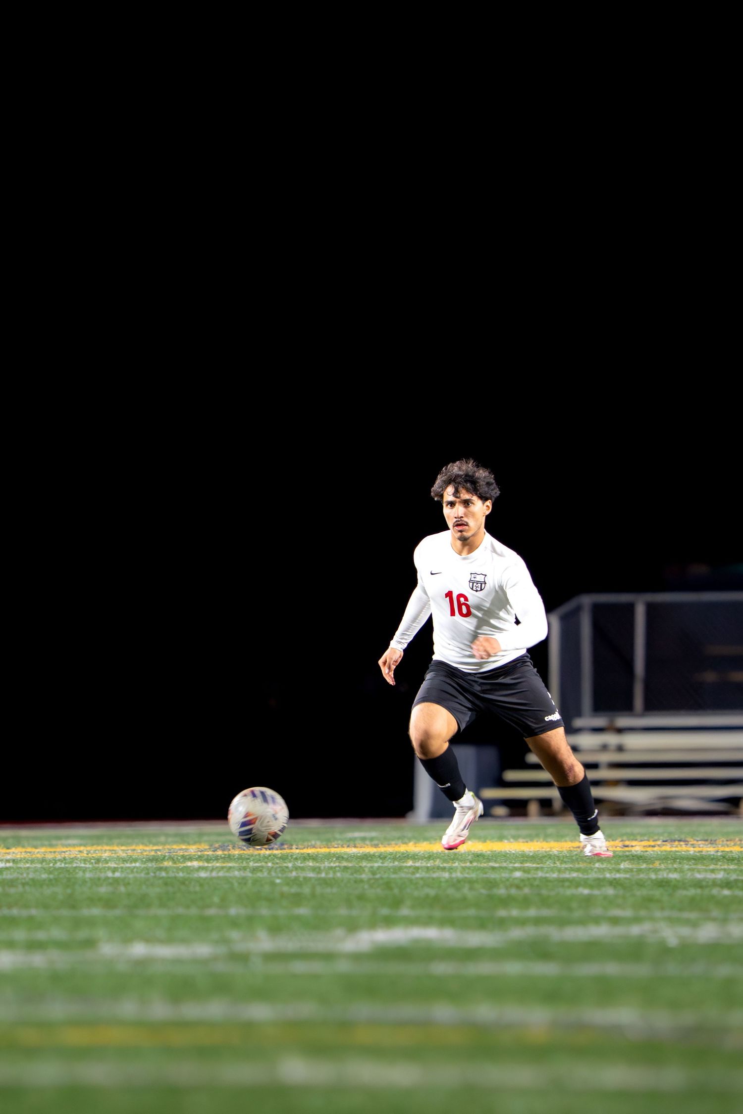 Soccer player in white uniform stretches on field during nighttime match.