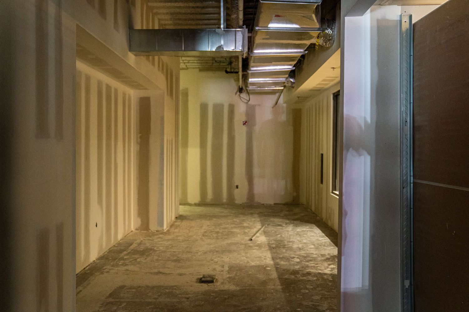 Long industrial hallway with fluorescent lighting and unfinished construction work.