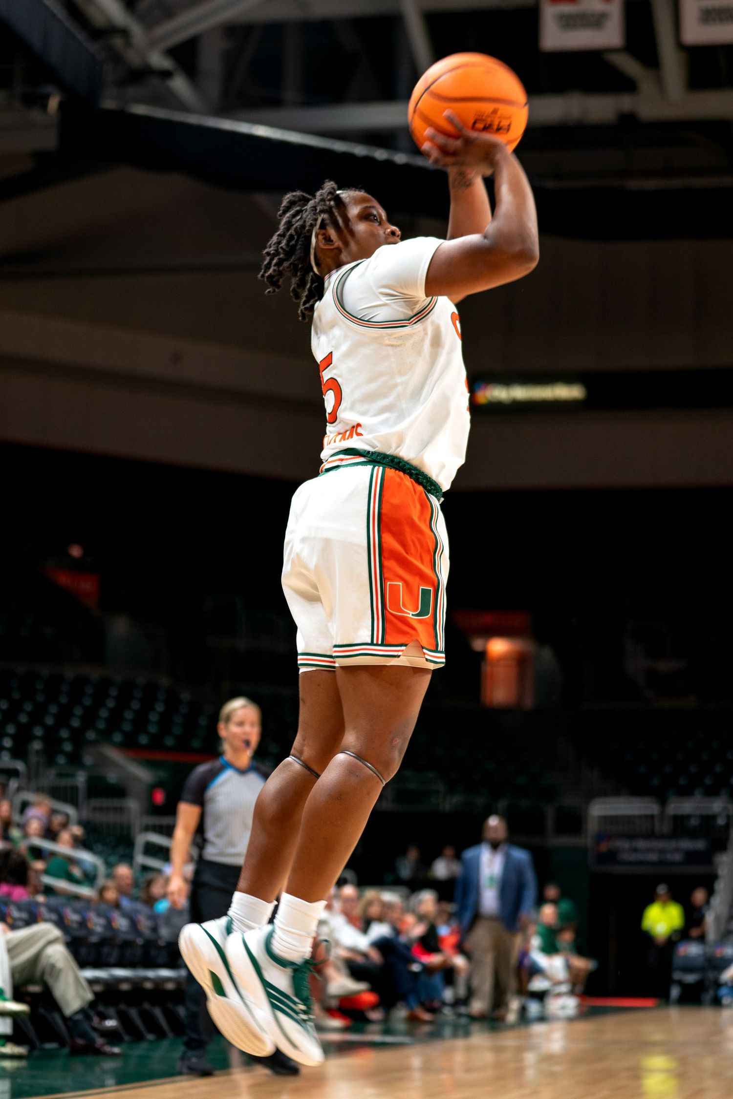 Basketball player in white Miami Hurricanes uniform jumps to make a shot during a game.