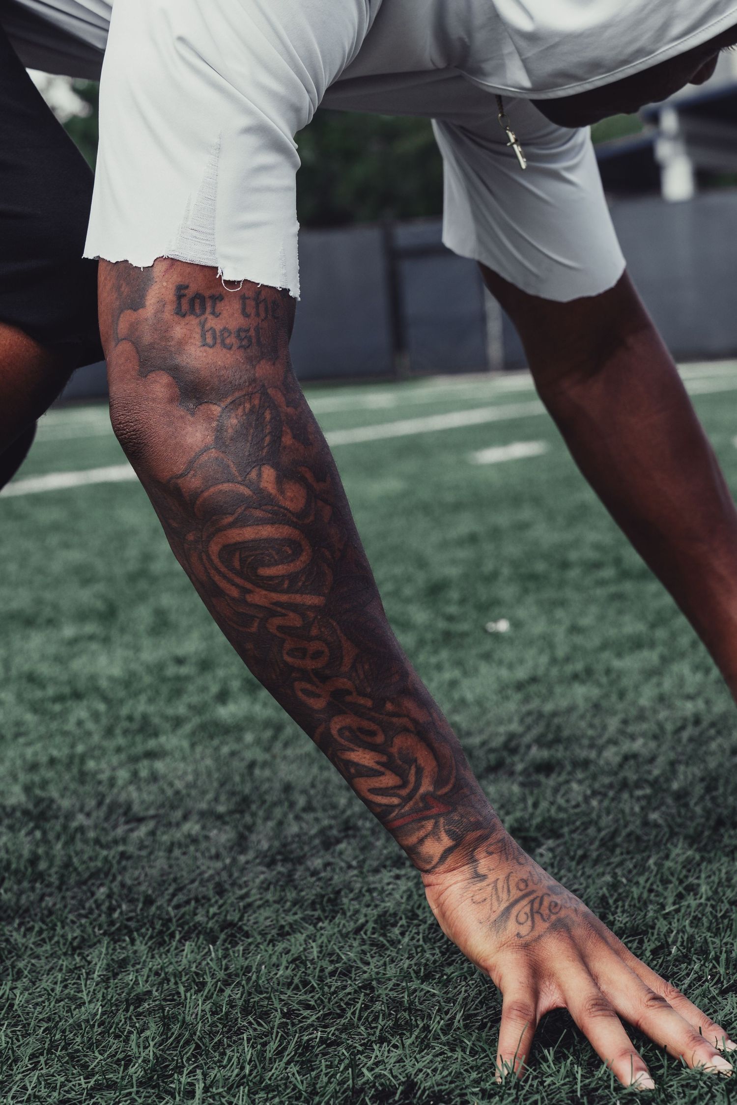 Close-up of a tattooed arm on a football field turf during an athletic workout session.