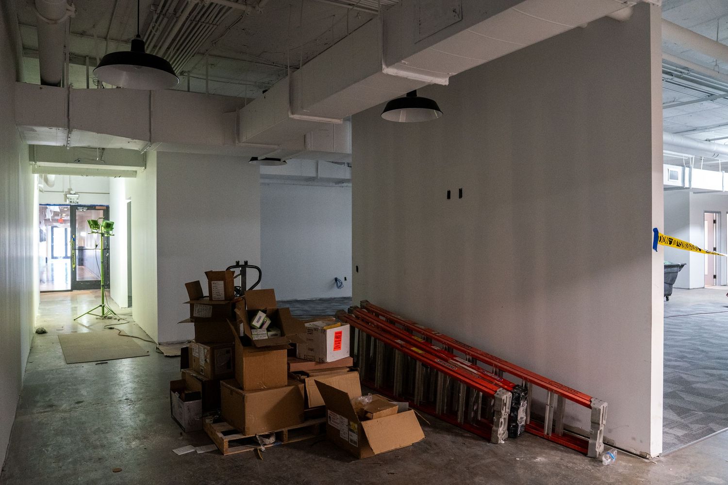 Unfinished commercial space with stacked boxes and construction equipment near white walls.