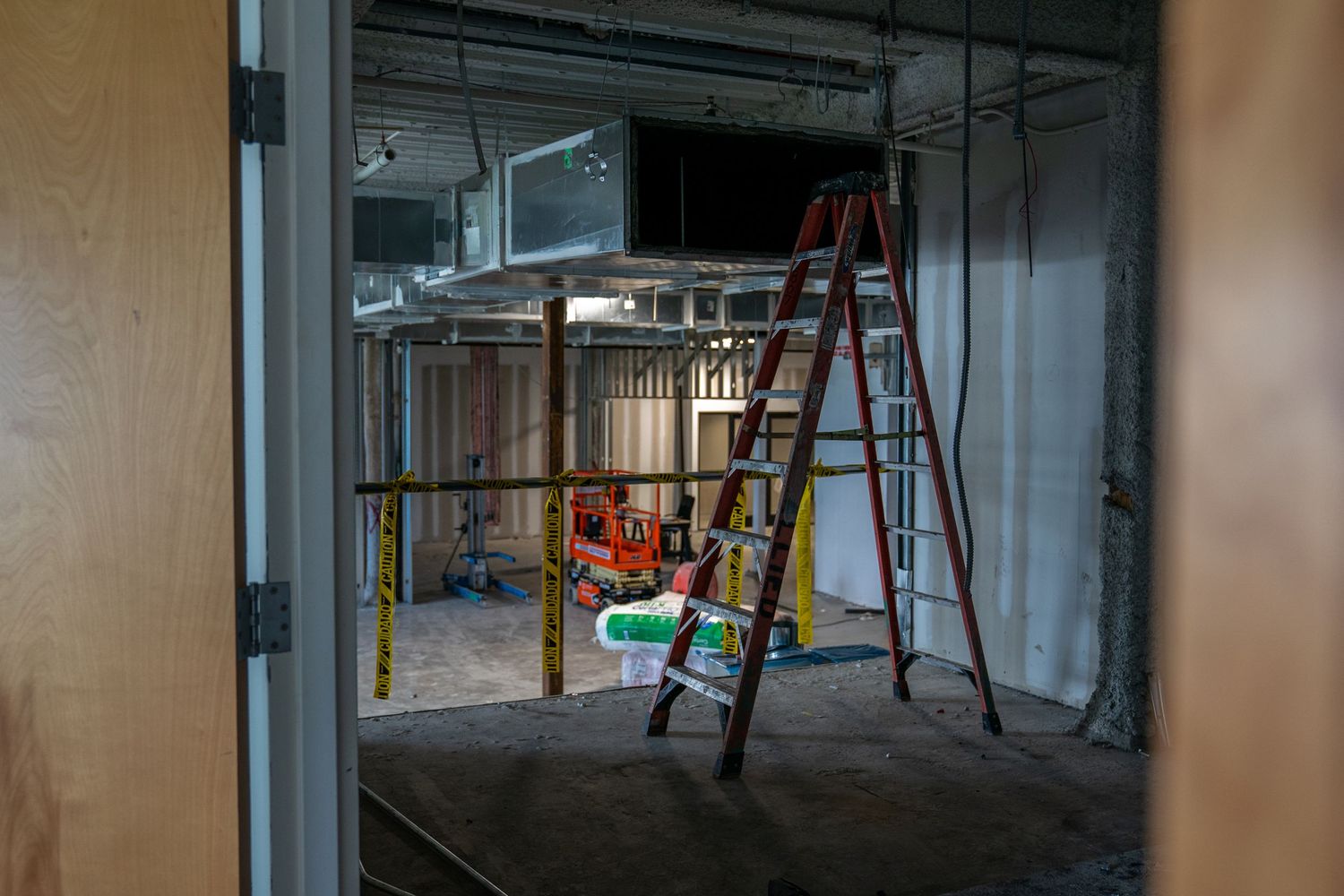 Panoramic view of unfinished commercial space with ladders and construction equipment.