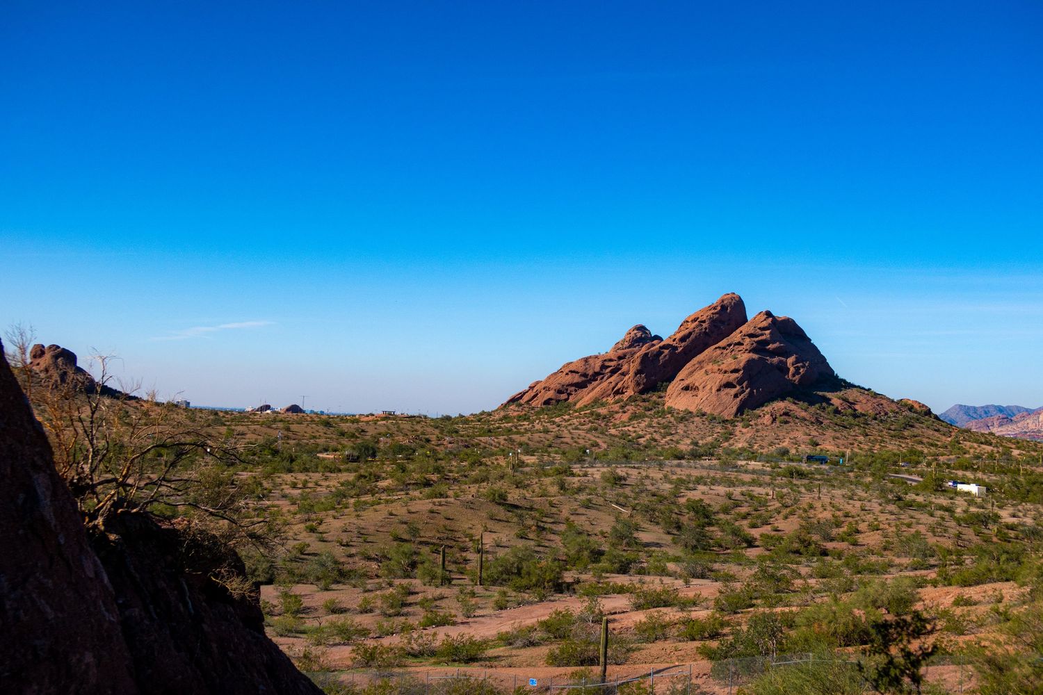 Red rock formations rise from the desert landscape under bright blue skies.