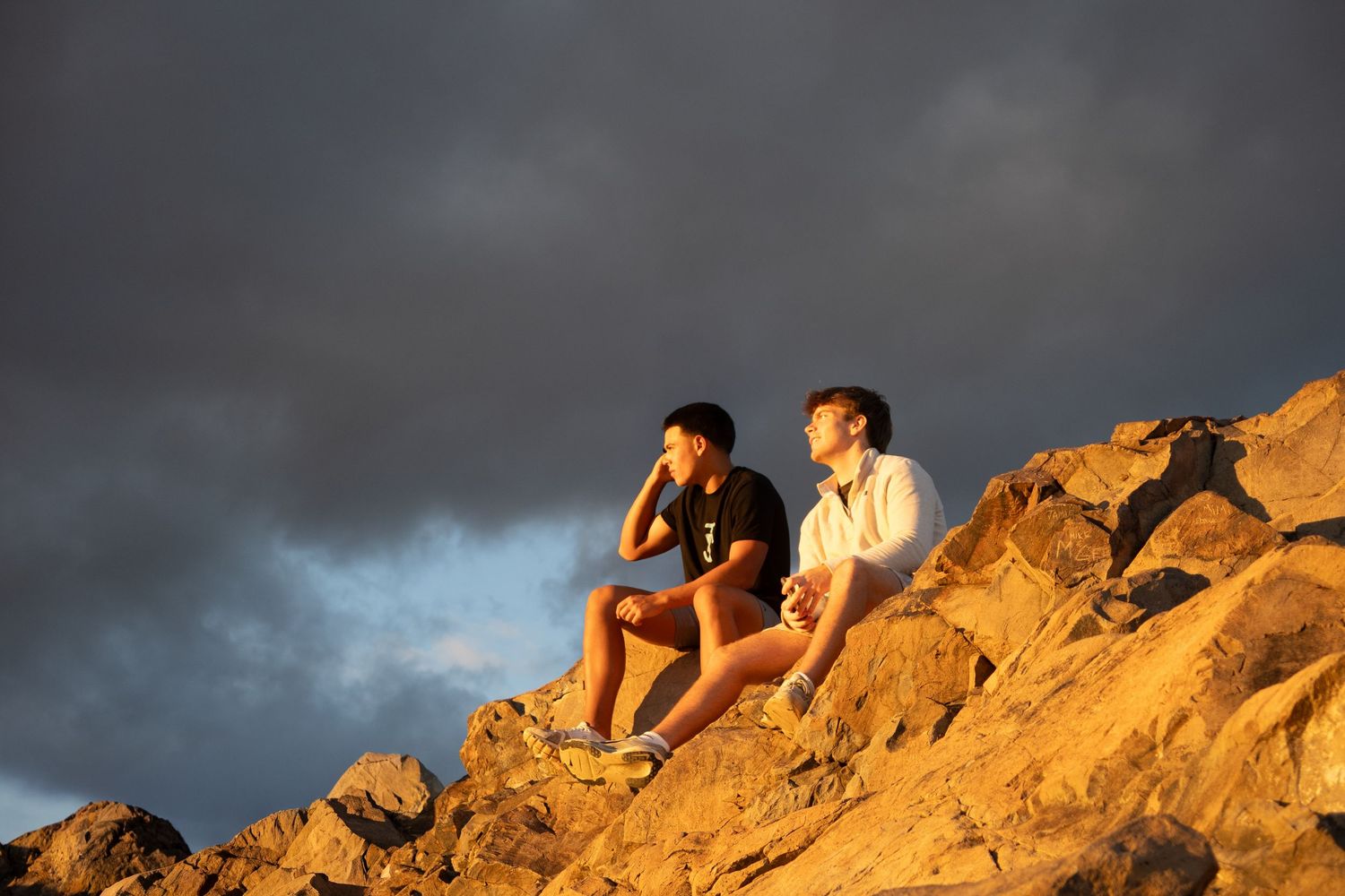 Silhouettes of people relaxing on rocky outcrop during golden hour.