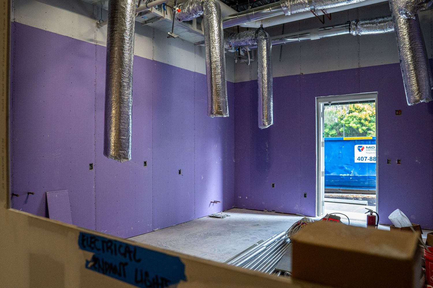 Purple-walled room under construction with exposed ceiling and natural light from windows.