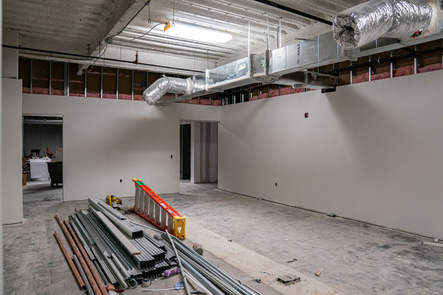 Interior construction site with exposed ceiling infrastructure and concrete flooring.