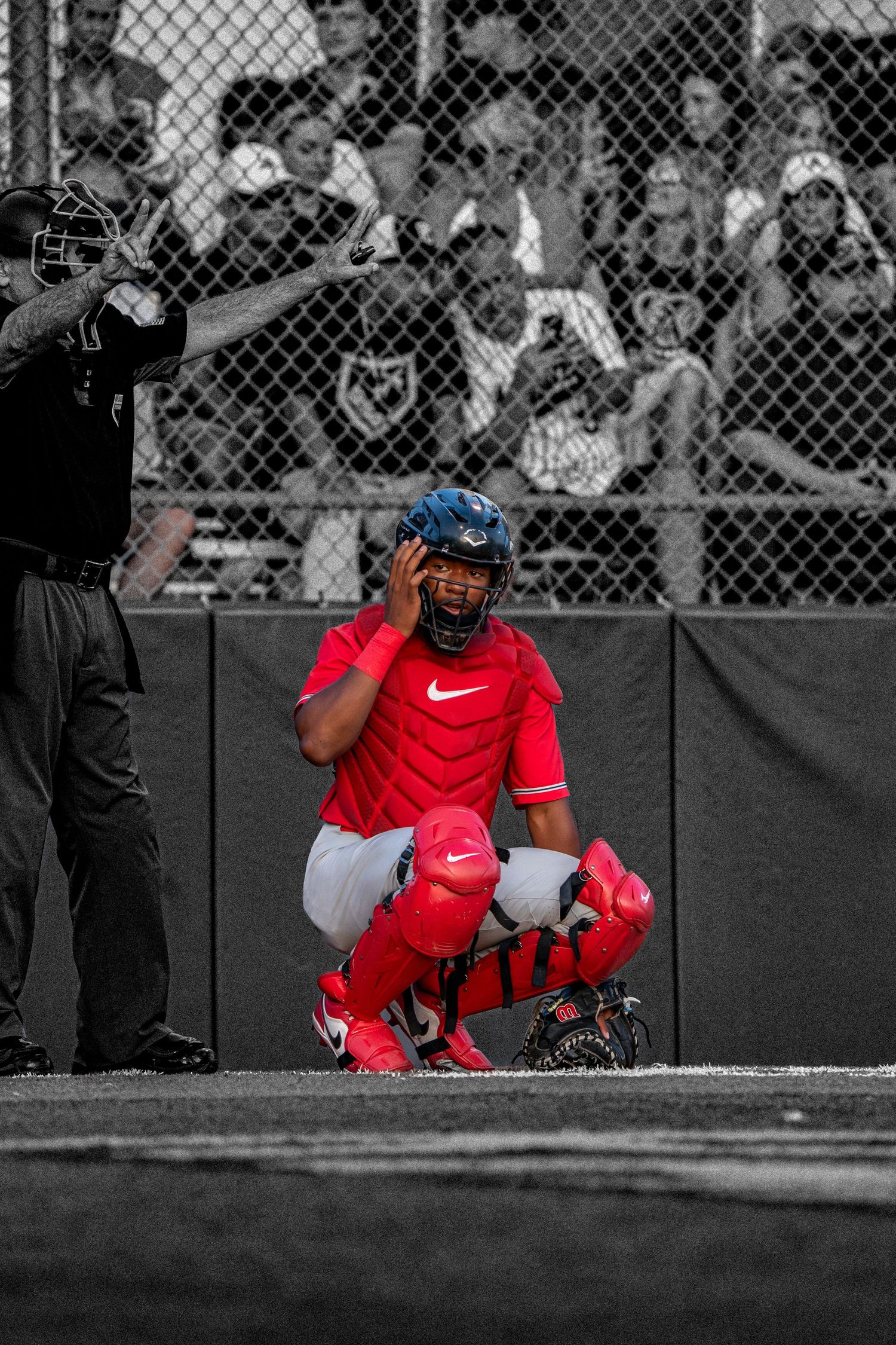 Baseball catcher in red uniform crouches behind home plate during a game.