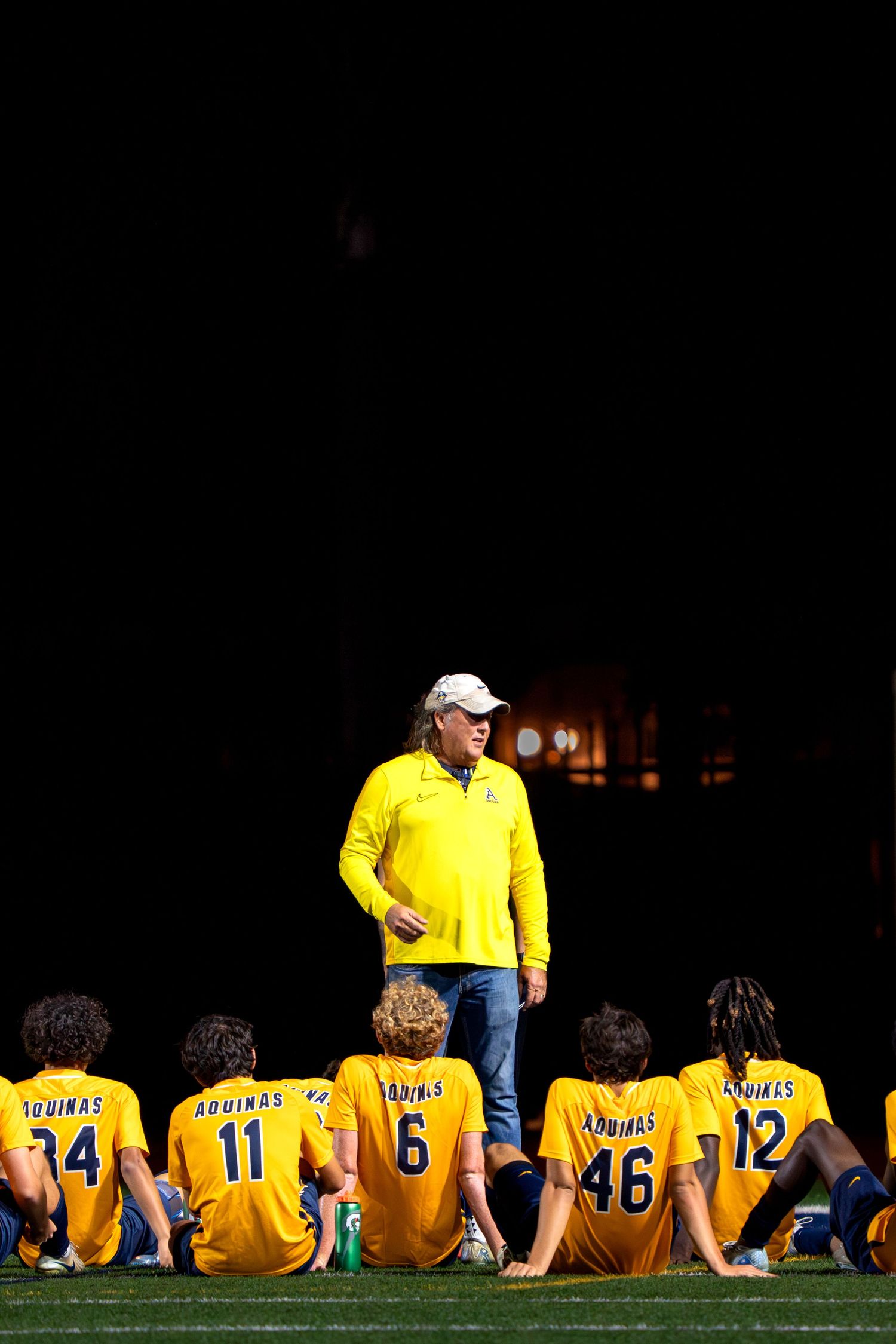 Soccer team in yellow jerseys sitting on sideline during game break.