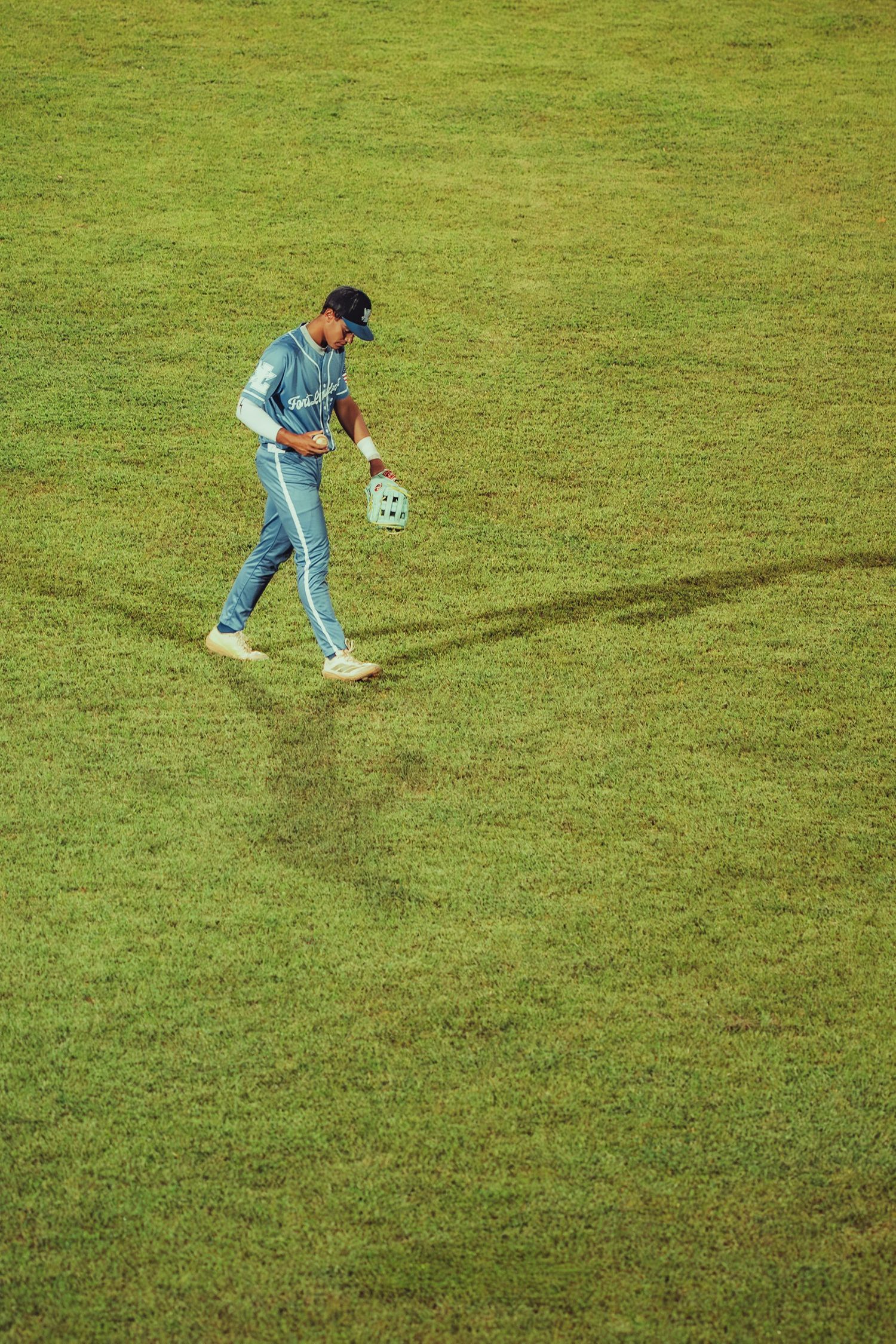 A baseball player walks across a green field carrying a helmet during a game.