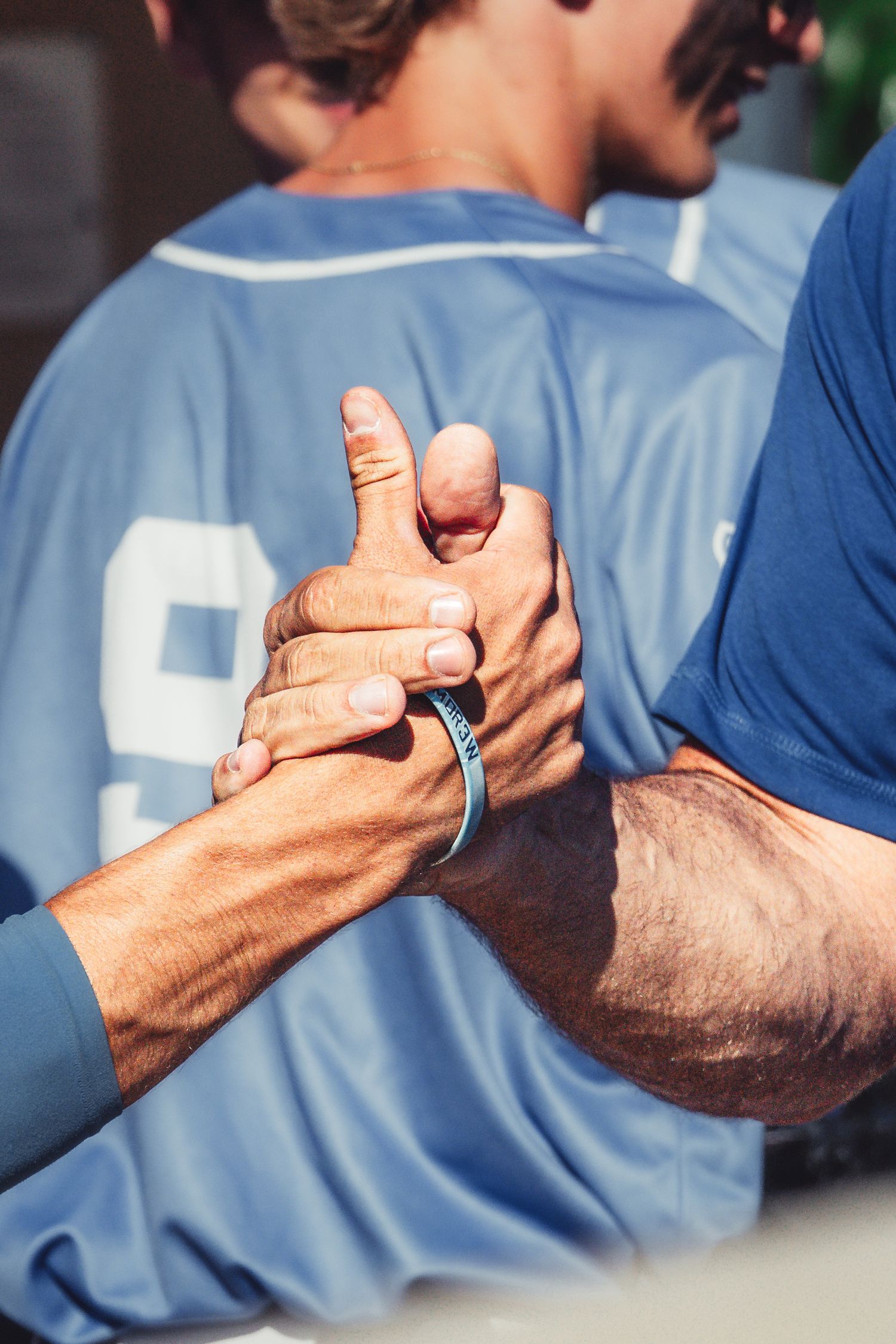 Two athletes in blue jerseys share a firm handshake after a competitive sports match outdoors.