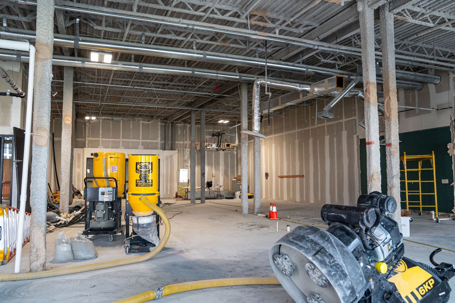 Industrial space showing construction progress with yellow safety barriers and exposed infrastructure.