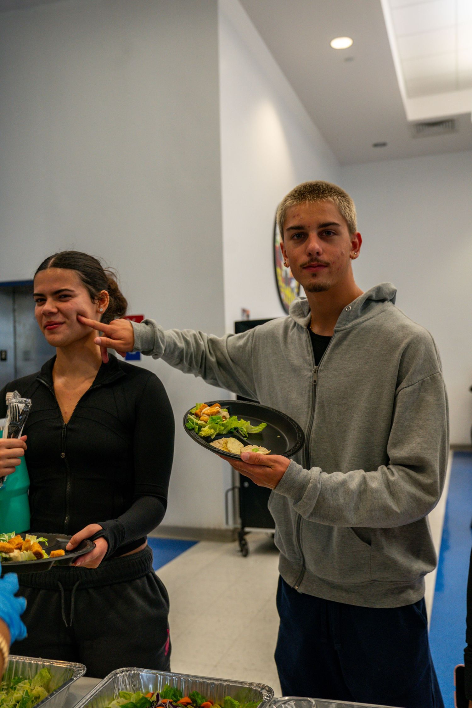 Students serving and enjoying food at a casual gathering in a classroom space.